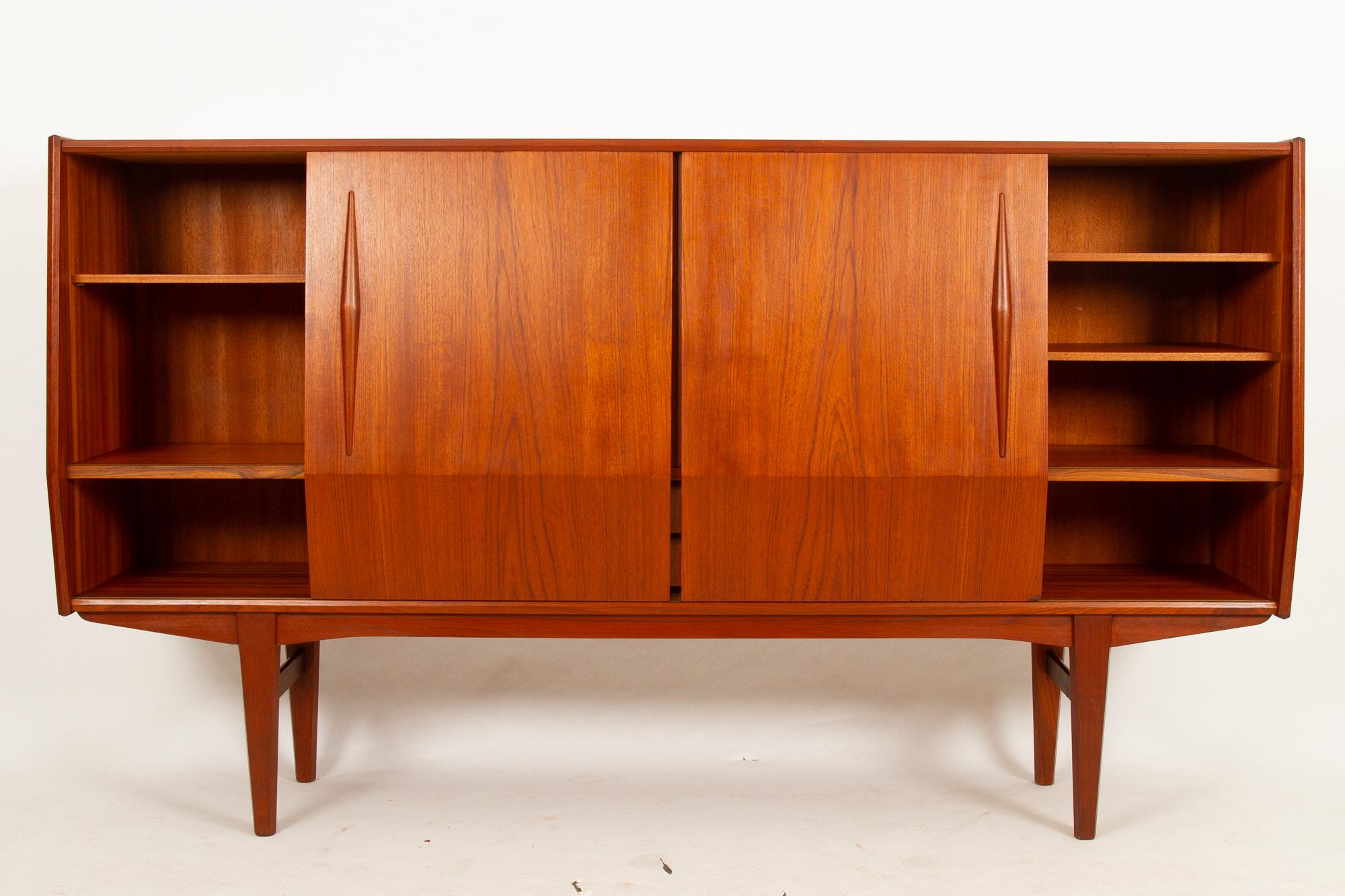 Danish teak sideboard 1960s.
Tall credenza with mirrored bar unit, shelves and drawers. Many beautiful details and loads of storage space. The bar unit features decorated mirror and curved shelves on brass pillars. Four small drawers with green
