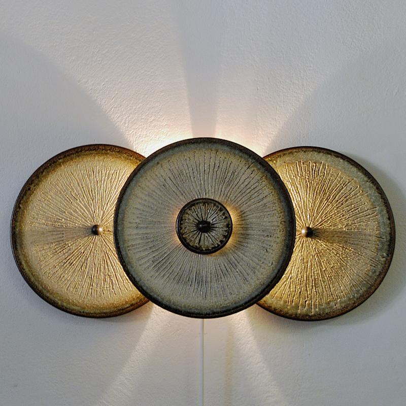 A stunning wall light sculpture of three ceramic plates by Noomi Backhausen and Poul Brandborg for Søholm Keramik, Bornholm Denmark in the 1960s. Beautifully glazed earth colored stoneware with rippled texture in front. Beautiful light flowing out