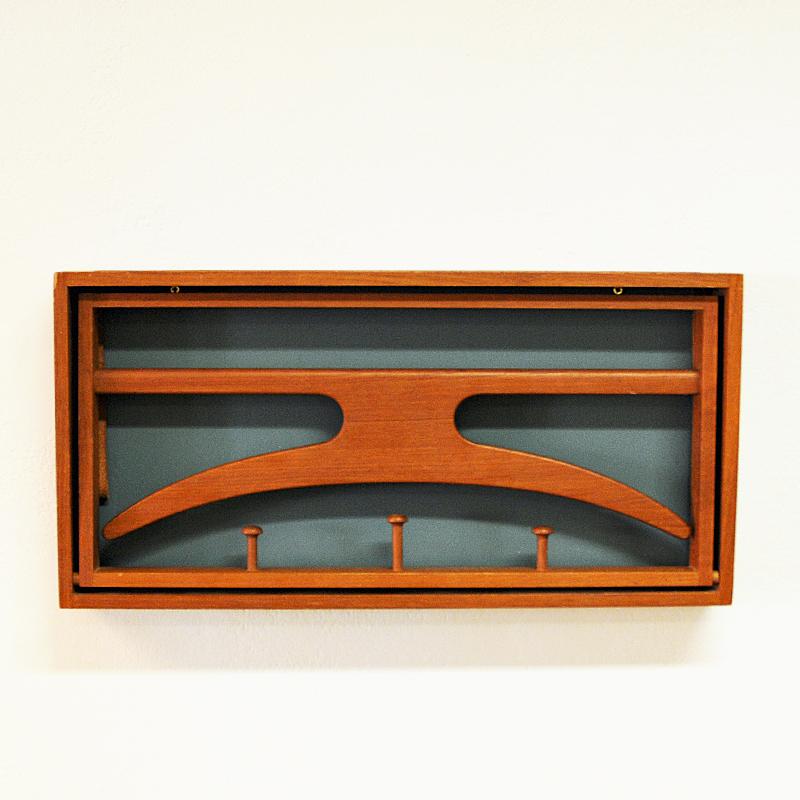 A wall-mounted valet/rack clothing hanger designed by Adam Hoff & Poul Østergaard and produced by Virum Møbelsnedkeri in Denmark during the late 1950s. Solid teak frame, 3 hangers and brown leather straps when unfolded. Back part of lacquered