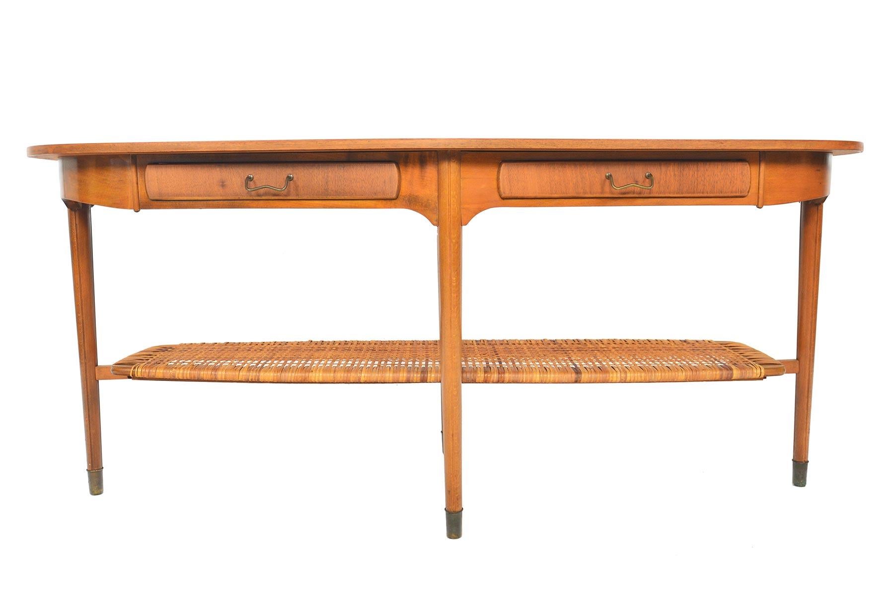 This gorgeous Danish modern walnut coffee table hails from the 1950s. Offering traditional detailing in a modern silhouette, this table offers elegance and exceptional storage! The walnut tabletop houses two drawers with brass pulls. The unique four