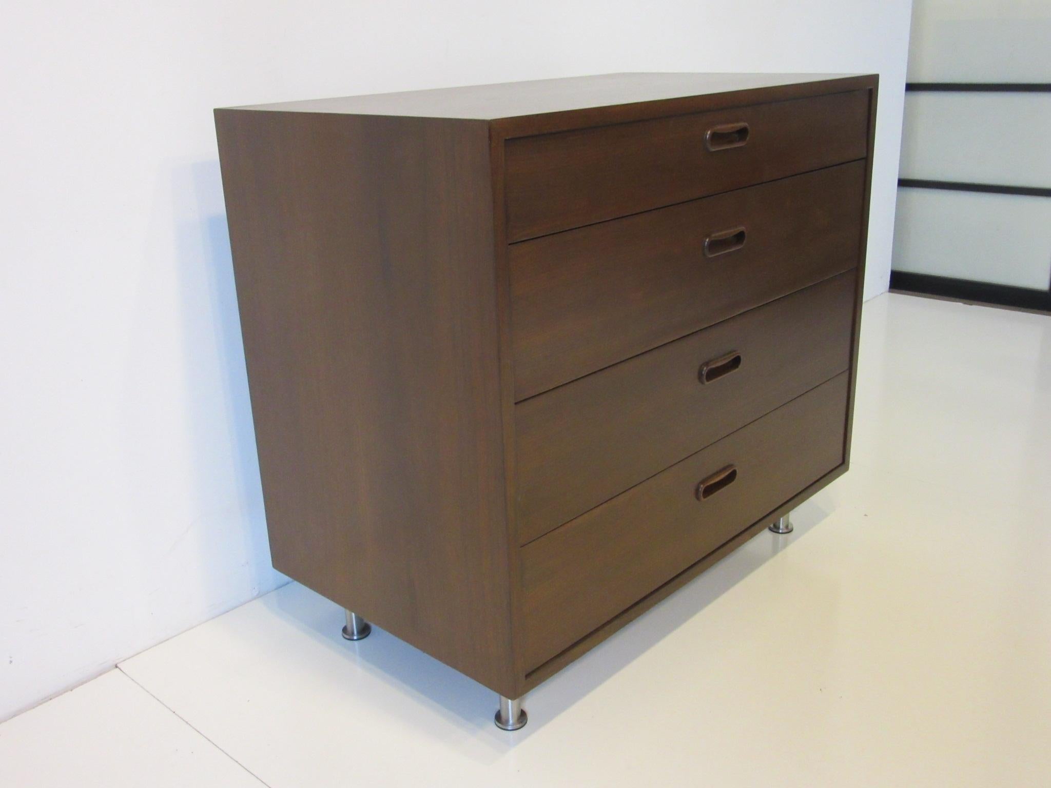 A dark walnut smaller sized four-drawer dresser chest with matching pulls sitting on brushed stainless steel adjustable legs, the backside is finished in the same walnut designed by Poul Cadovius for Cado with replaced legs.