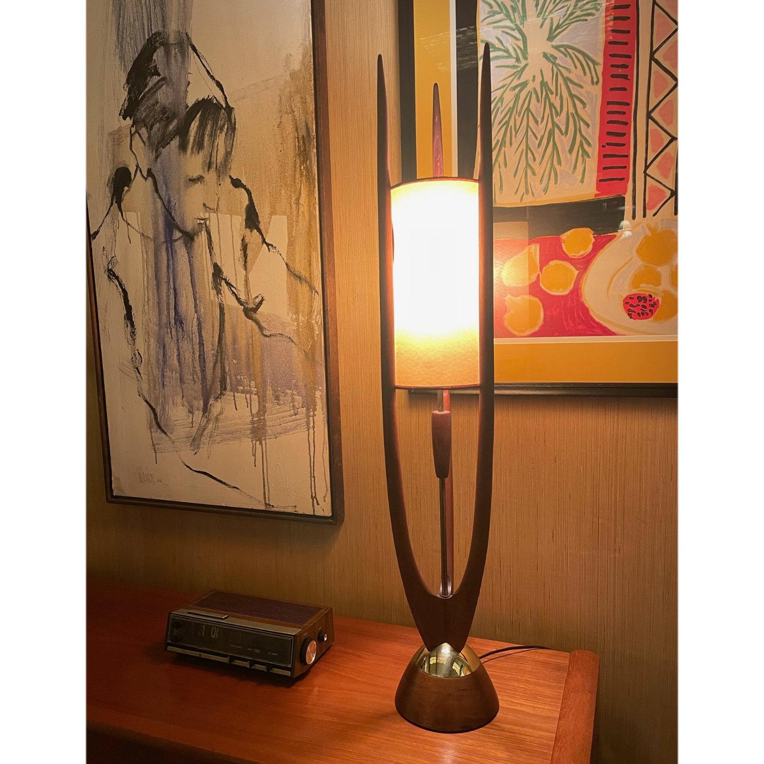 Stunning sculptural Mid-Century Modern table lamp designed in the manner of Modeline. The lamp appears to be solid walnut or teak, accented with brass at the base. The three-point trident structure cradles the original cylinder lamp shade at center.