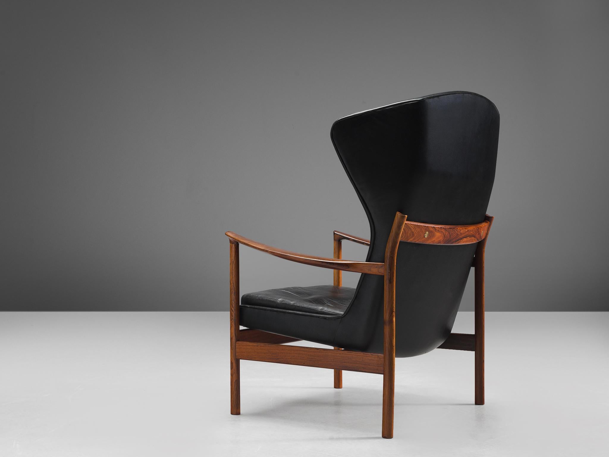 Danish cabinetmaker, wingback easy chair, rosewood frame, black leather, Denmark, 1960s.

This sculptural wingback easy chair is made with a rosewood frame and have brass fittings. The seat has a black upholstered shell that floats within the