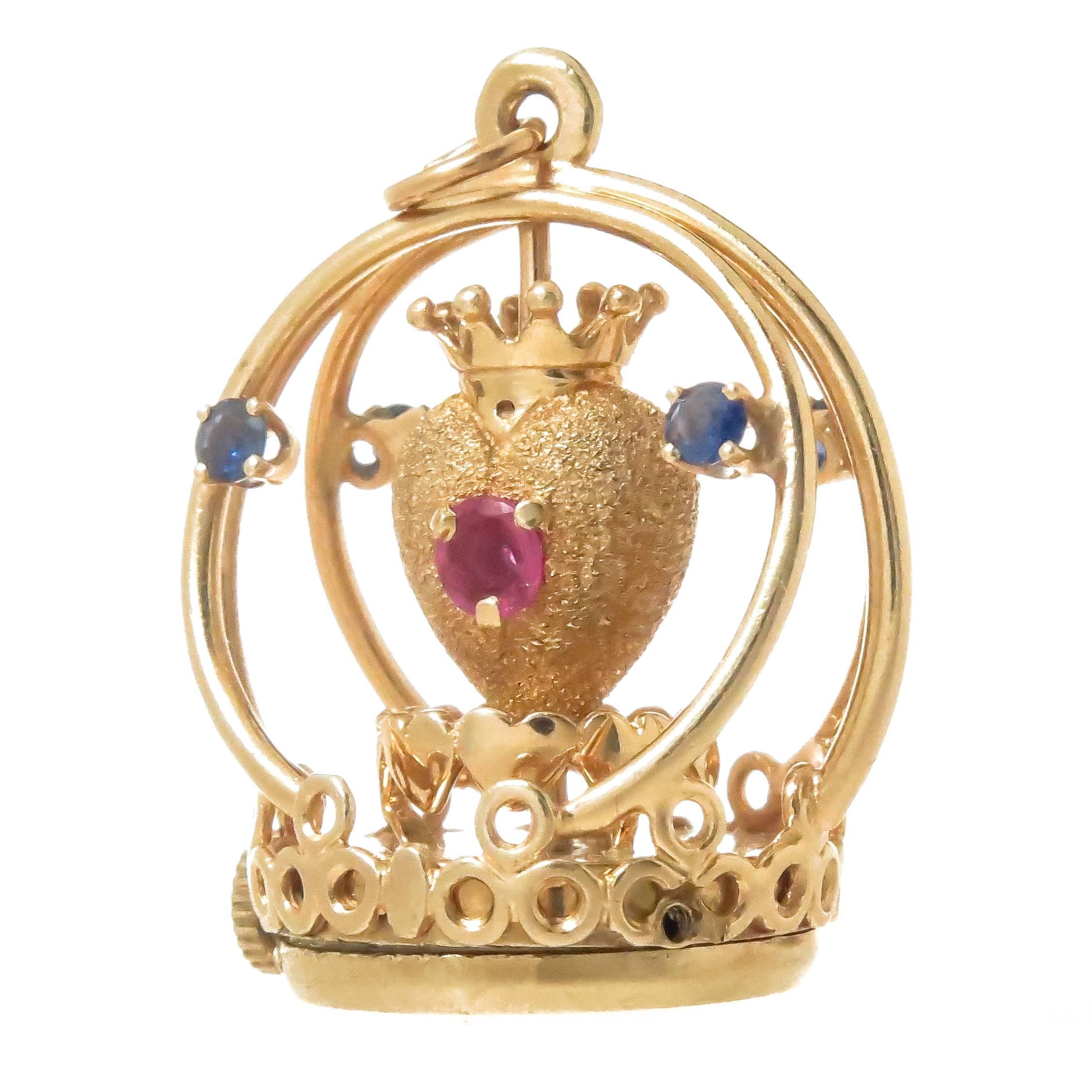 Circa 1960s Henry Dankner 14K yellow Gold Sacred heart Charm, measuring 1 1/4 inch in height and 1 inch wide, set with Rubies and Sapphires. The mechanical wind up mechanism that enables the Heart in the center of the charm to spin around has