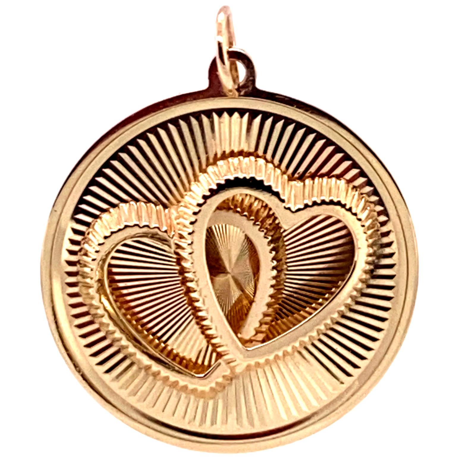  Romantic double-heart charm.. Made and signed by HENRY DANKNER & SONS.  Two three-dimensional intertwined fluted hearts applied on a background of  engraved rayed lines.  14K yellow gold.  In pristine condition. 1 1/16