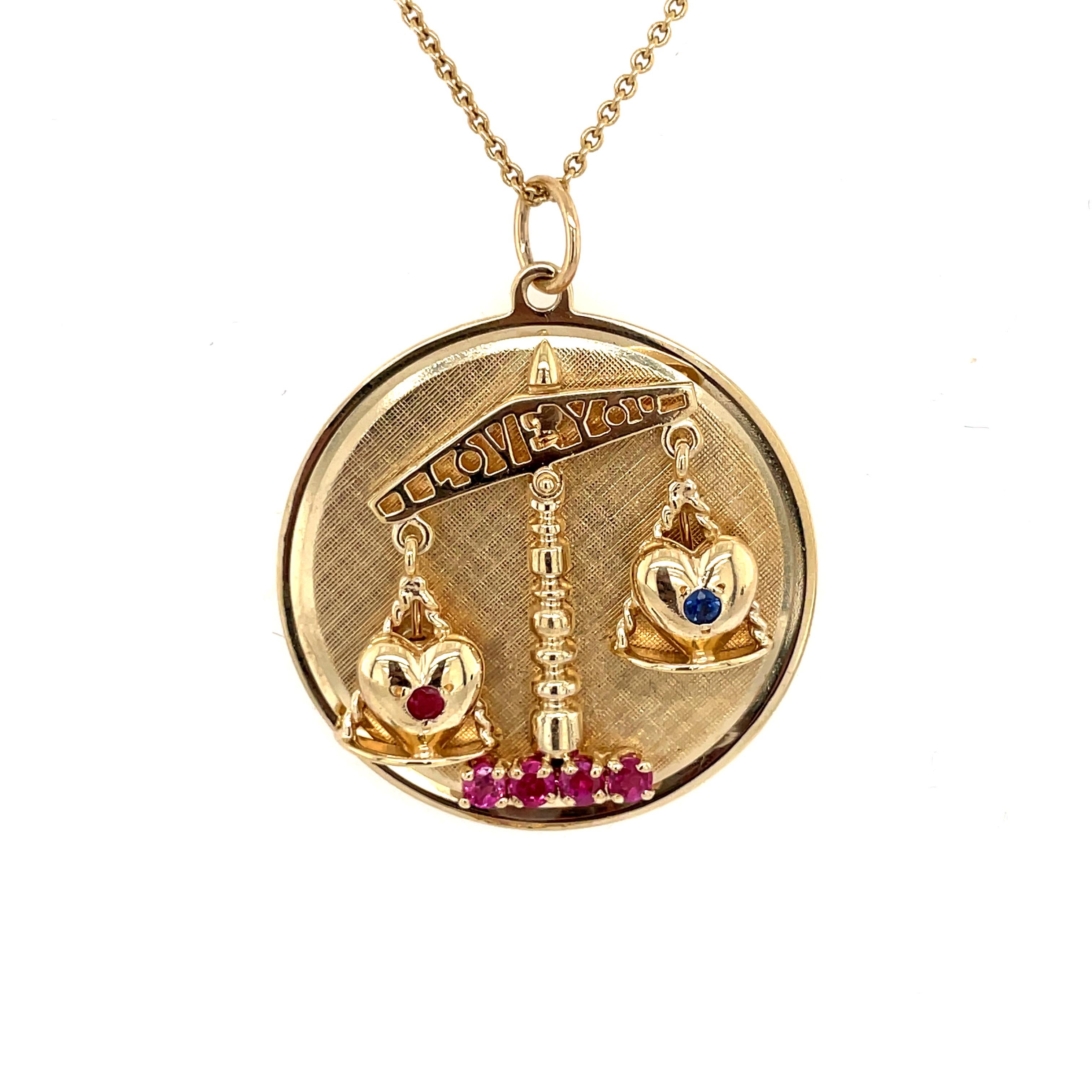 The ultimate love charm:   a round disc with a shiny gold border and textured gold background.  Made and signed by HENRY DANKNER & SONS.
In the center, there is an applied scale of justice set with two shiny gold hearts.   One heart is set with a
