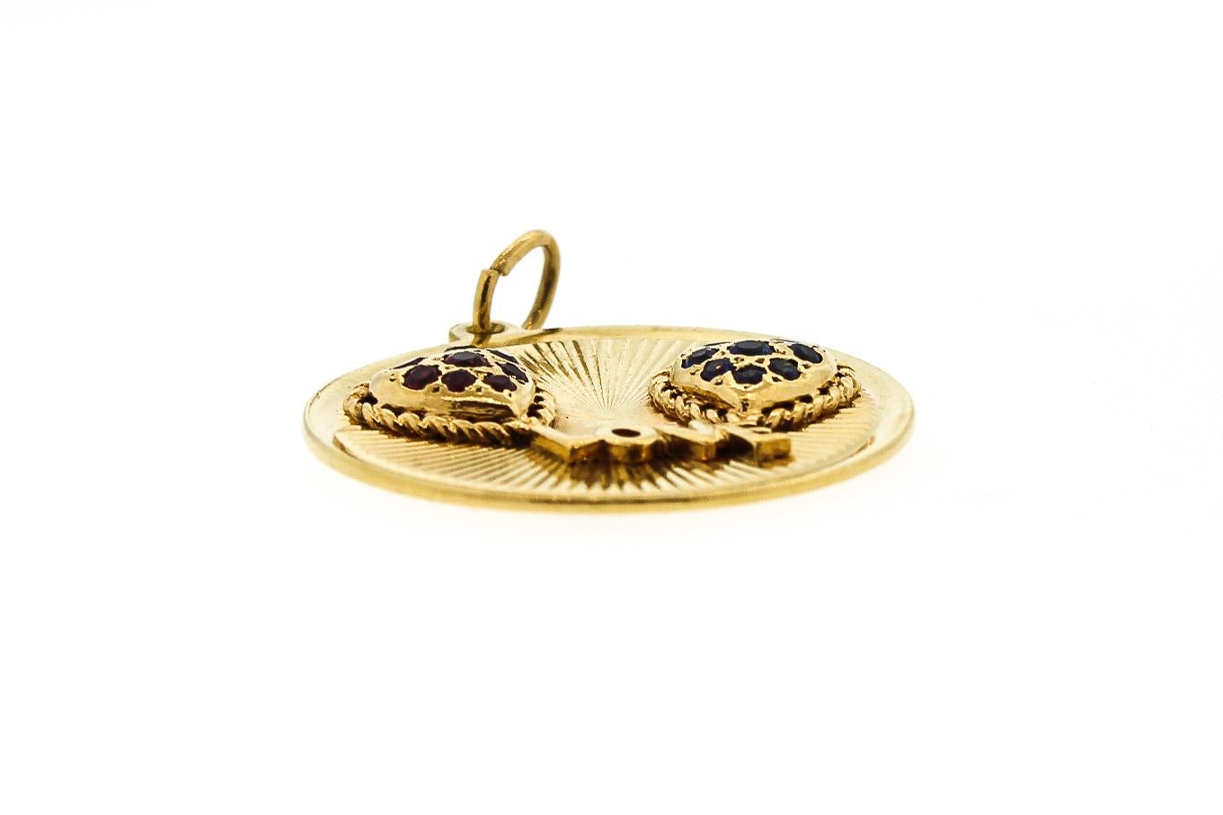 Puffy ruby and sapphire set hearts are connected by LOVE on this 14k yellow gold disc charm by Dankner. The charm is about 1.1 inches in diameter and the front is ridged in texture. The charm is whimsical like two balloons connected together by