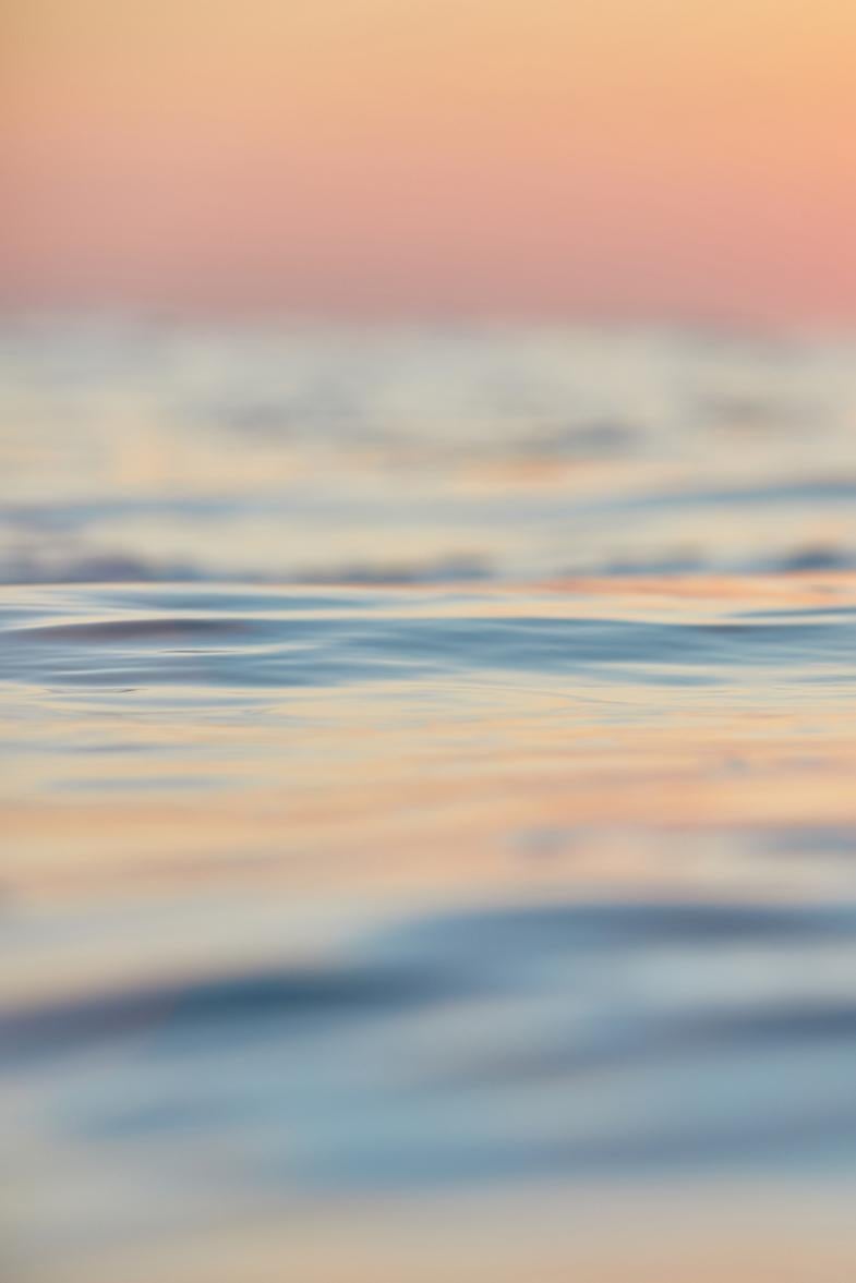 Auf diesem Foto spiegelt sich ein rosafarbener und goldgelber Sonnenuntergang auf der Oberfläche eines ruhig schimmernden Ozeans, wobei sich Gelb- und Orangetöne zwischen dem Blau des Himmels und dem Saphirblau des Wassers brechen. Großformatige