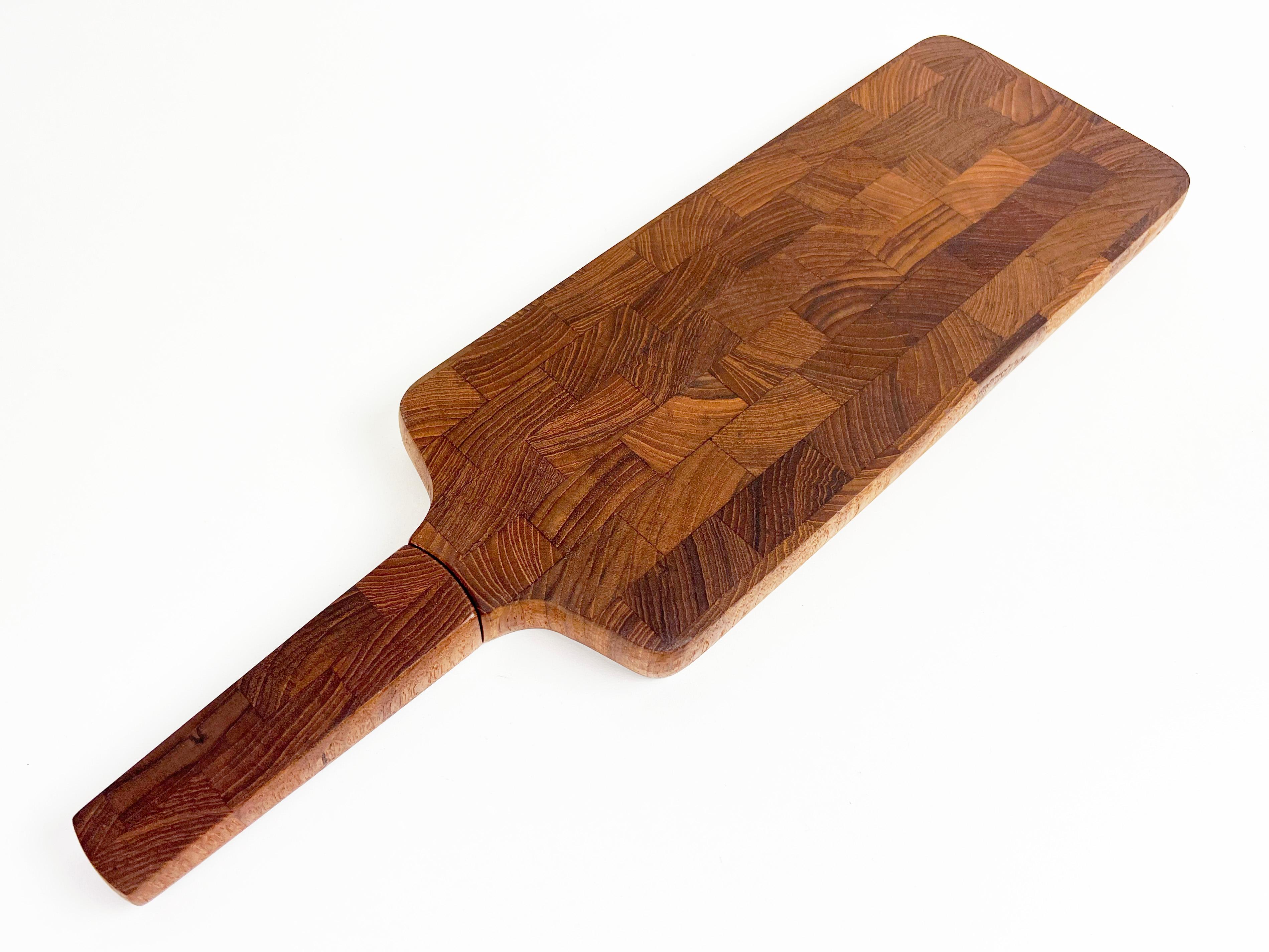 Vintage paddle shaped serving/cutting board with a built-in stainless steel serrated knife hidden in the handle. Constructed of solid end-grain teak. 

Designer: Jens Quistgaard

Manufacturer: Dansk

Dimensions: 19.25
