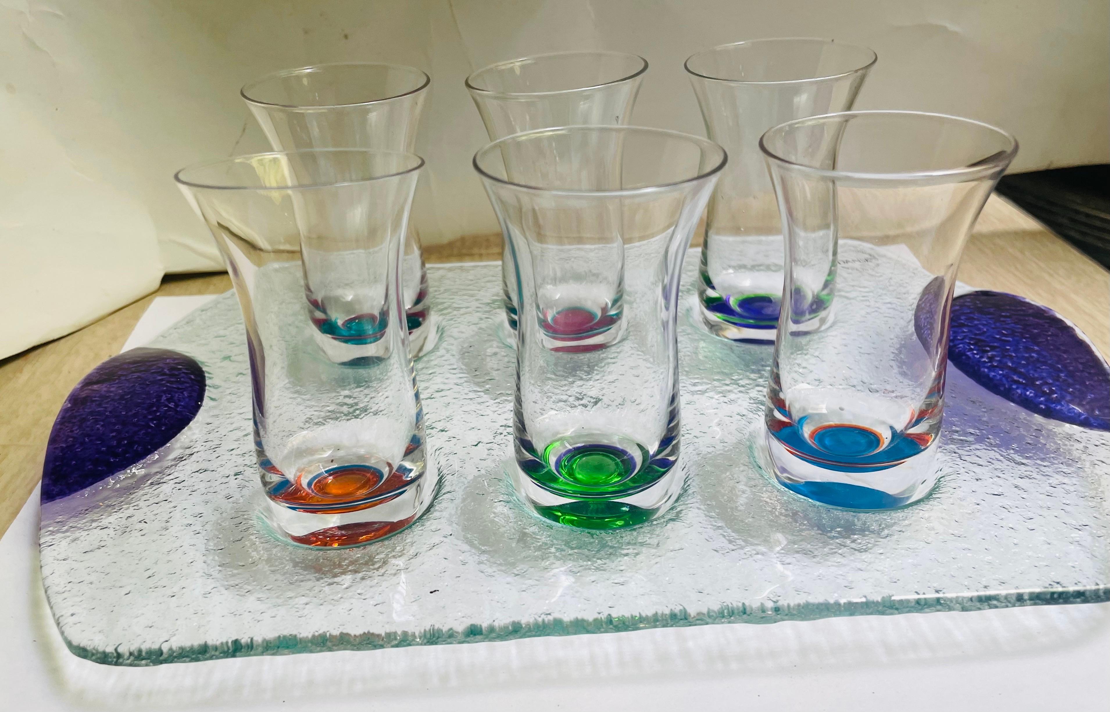 What a great looking modern shot glass and serving tray set in the wonderful Dansk style. The mottled textured tray has purple colored handles and the shot glasses each have two colors in their base. 

The tray measures about 10 inches wide and 6