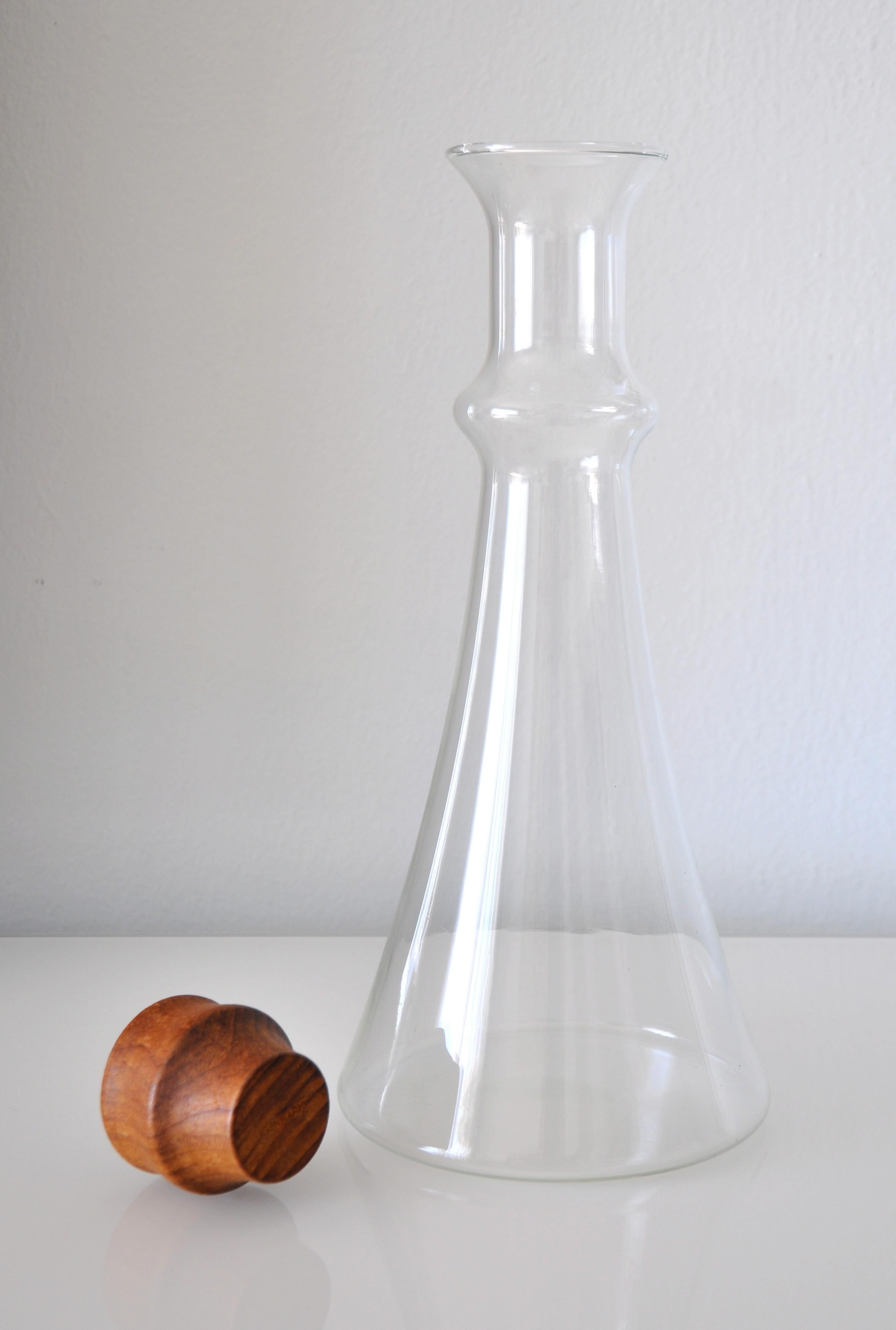 Hergestellt in Dänemark. Vintage-Glaskaraffe, entworfen von Gunnar Cyrén, um 1980. Der hohe, becherförmige Krug mit dem geschnitzten Teakholzstopfen ist die stilvolle Art, Wein oder Wasser zu servieren. Die Karaffe fasst 1,5 Liter.