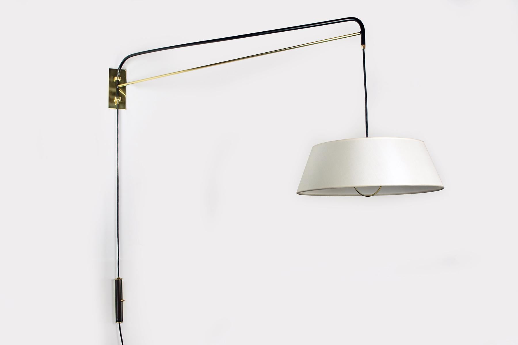 This graceful wall sconce is handcrafted by Bourgeois Boheme Atelier. It is made with a black enamel finish and polished brass. An elegant linen shade diffuses a soft light. This fixture is adjustable, the switched counter weight system allow for