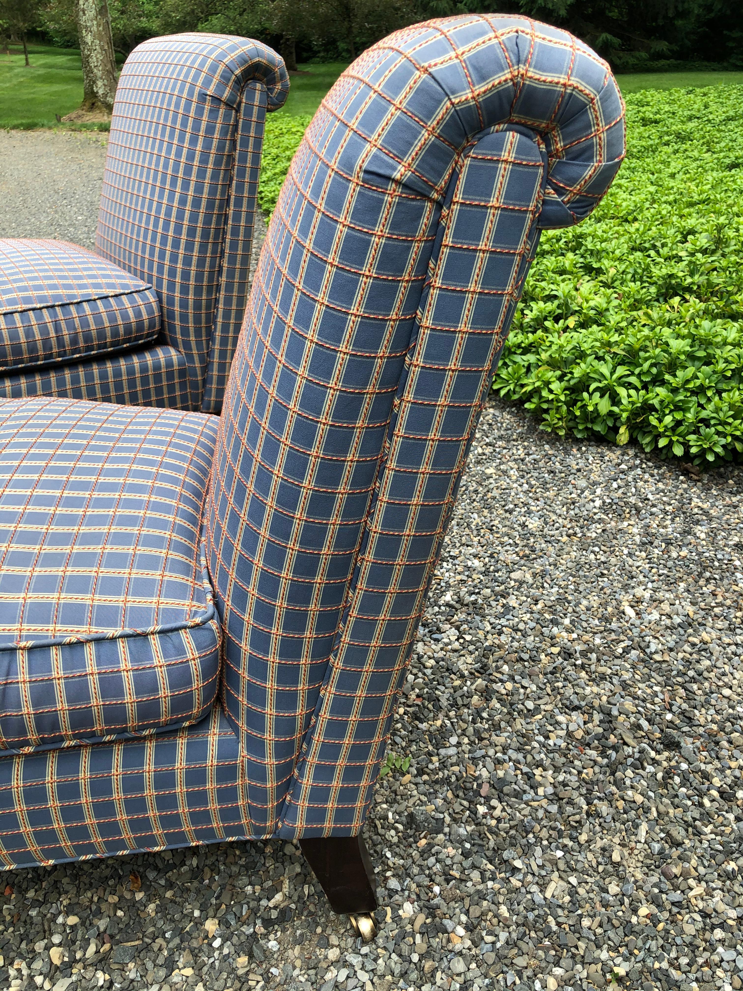 A very handsome pair of slipper chairs by Lee Jofa upholstered in a cornflower blue plaid with gold and persimmon threading and cushions that are down and feather filled. The front legs are turned mahogany on casters, while the rear legs are splayed