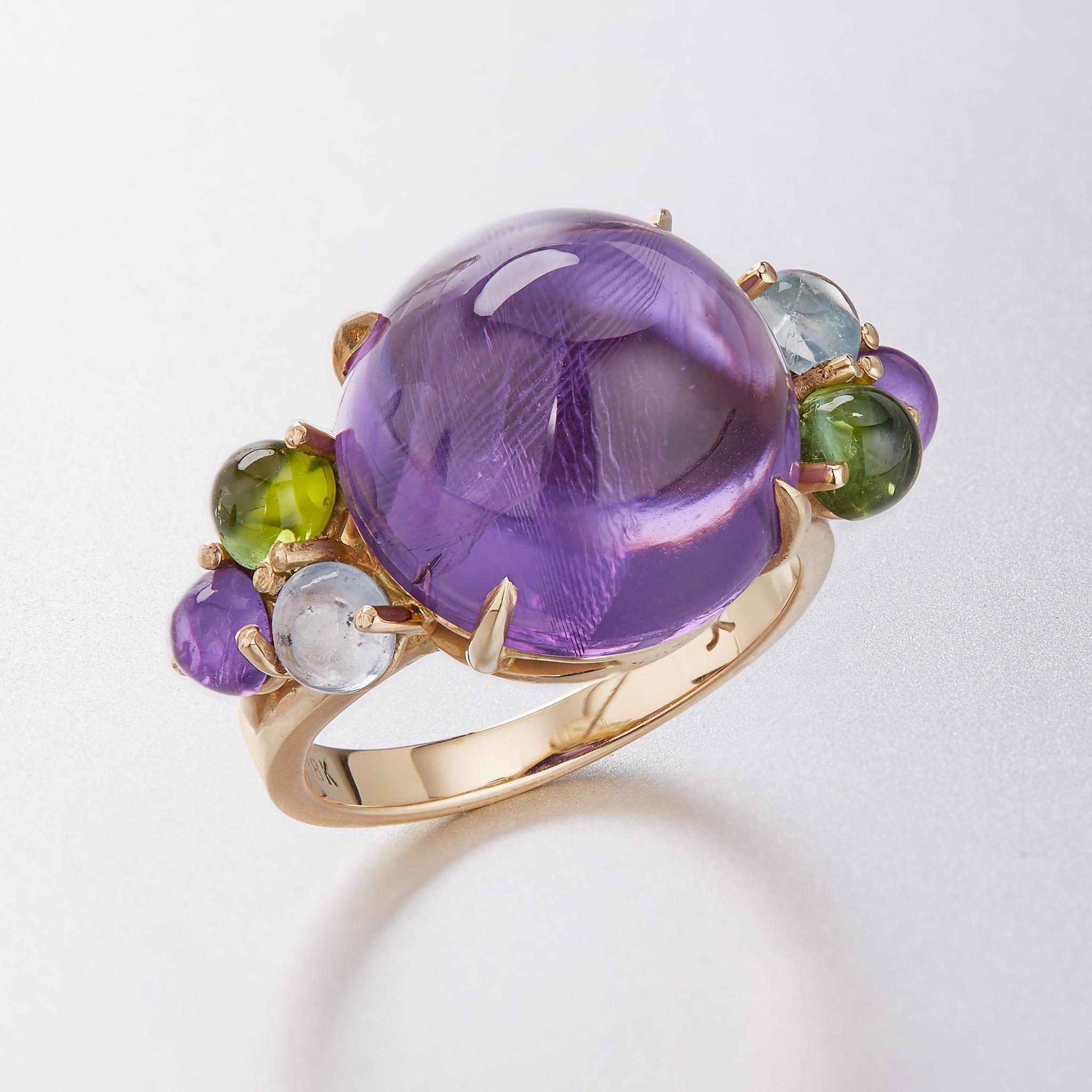 An impressive cocktail ring featuring a vibrant 14mm round cabochon amethyst center.  Complimented by a trio of gemstones on both sides with lush green tourmaline, baby blue aquamarine, and matching amethyst.

This ring can be sized to fit your