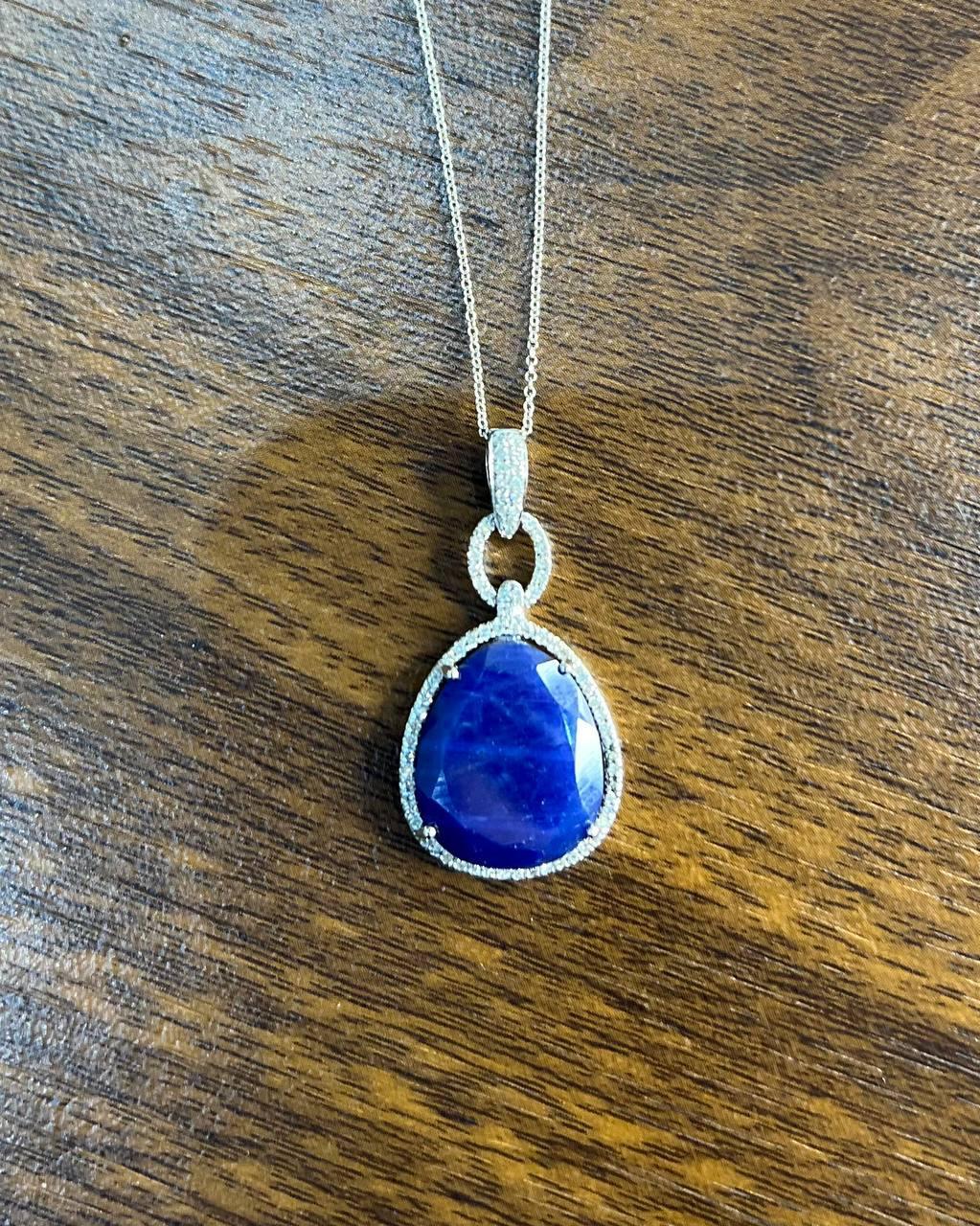 This exquisite necklace features a striking pendant.

The pendant showcases a deep dark blue sapphire in faceted cabochon slice, encircled by a halo of shimmering diamonds.

Expertly crafted with a delicate chain. 14K Whit Gold

A piece that