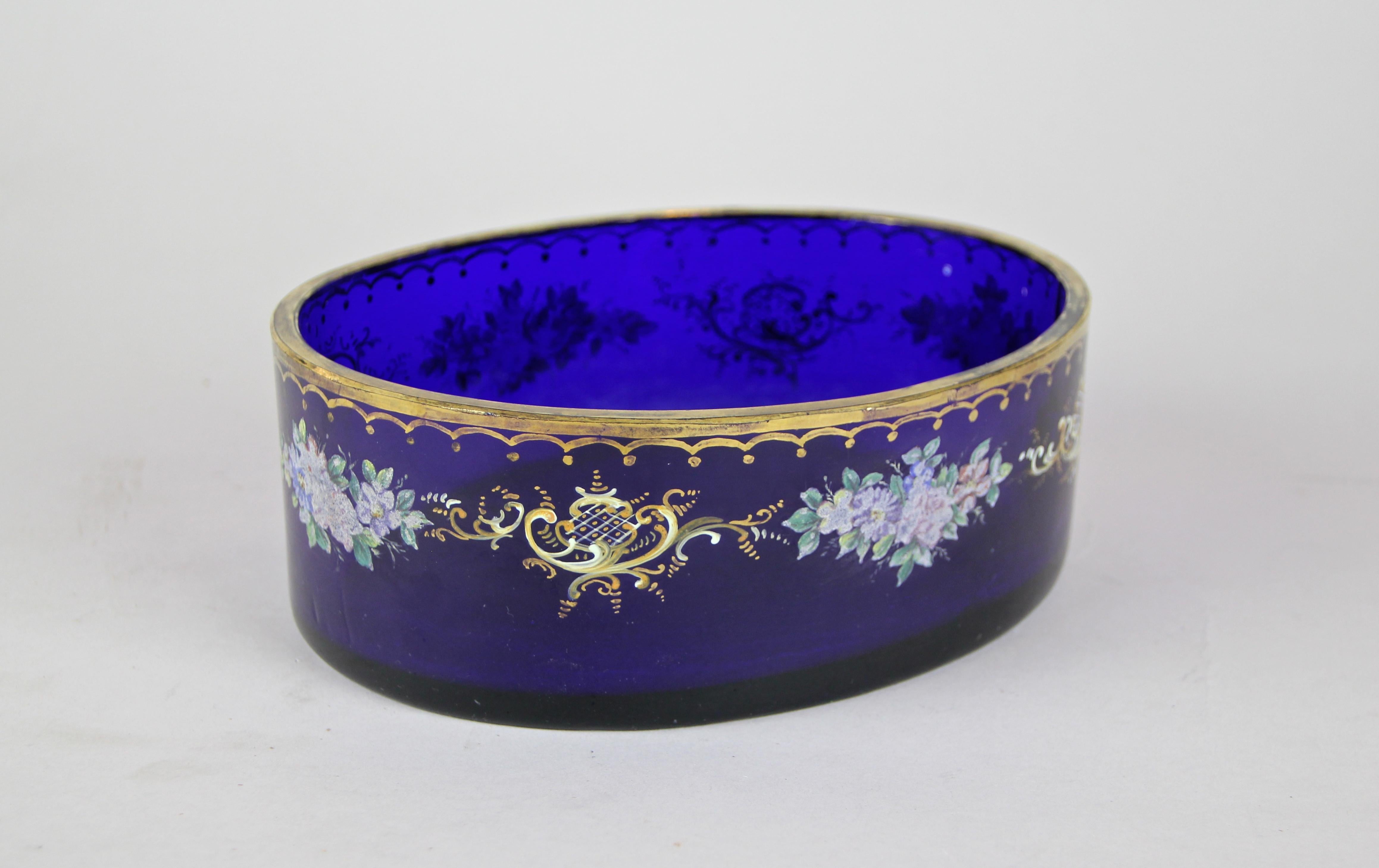 Enchanting dark-blue glass bowl from the famous Austrian Biedermeier era, circa 1840. The oval shaped glass bowl is adorned by elaborately hand painted flowers and other artfully designed elements. The golden upper edge builds a nice contrast to the