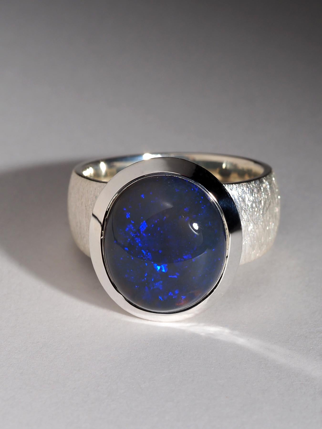 Dieser auffällige Ring besteht aus einem dunklen, natürlichen australischen Opal mit intensivem blauem Schimmer und einem raffinierten Pinfire-Muster. Der Opal misst 12 × 14 mm (0,47 × 0,55 Zoll) und wiegt 10,75 Karat. Er bietet ein lebhaftes,