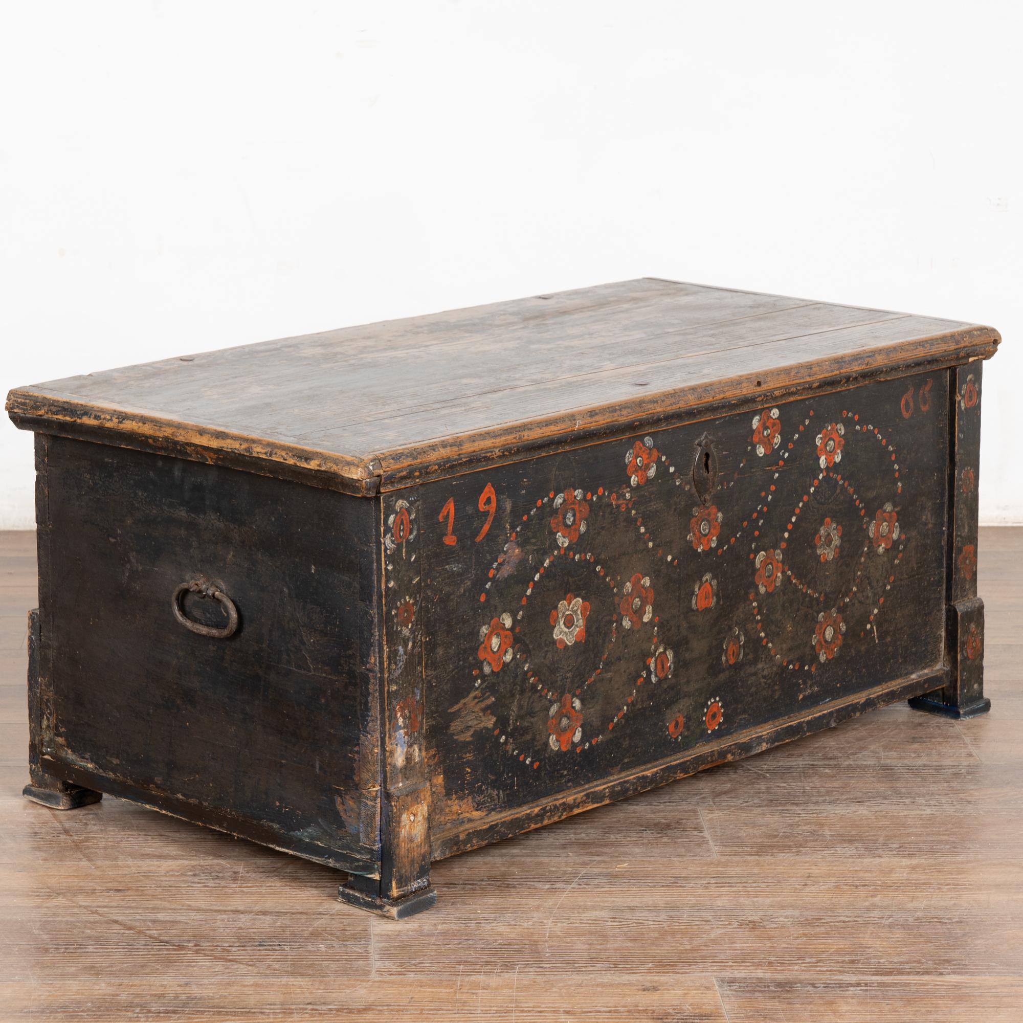 La finitura verniciata è tutta originale su questo baule rustico. Il colore dello sfondo è un blu scuro, che sembra quasi nero con una certa illuminazione.
I fiori erano un abbellimento tradizionale, come si vede sulla parte anteriore di questo