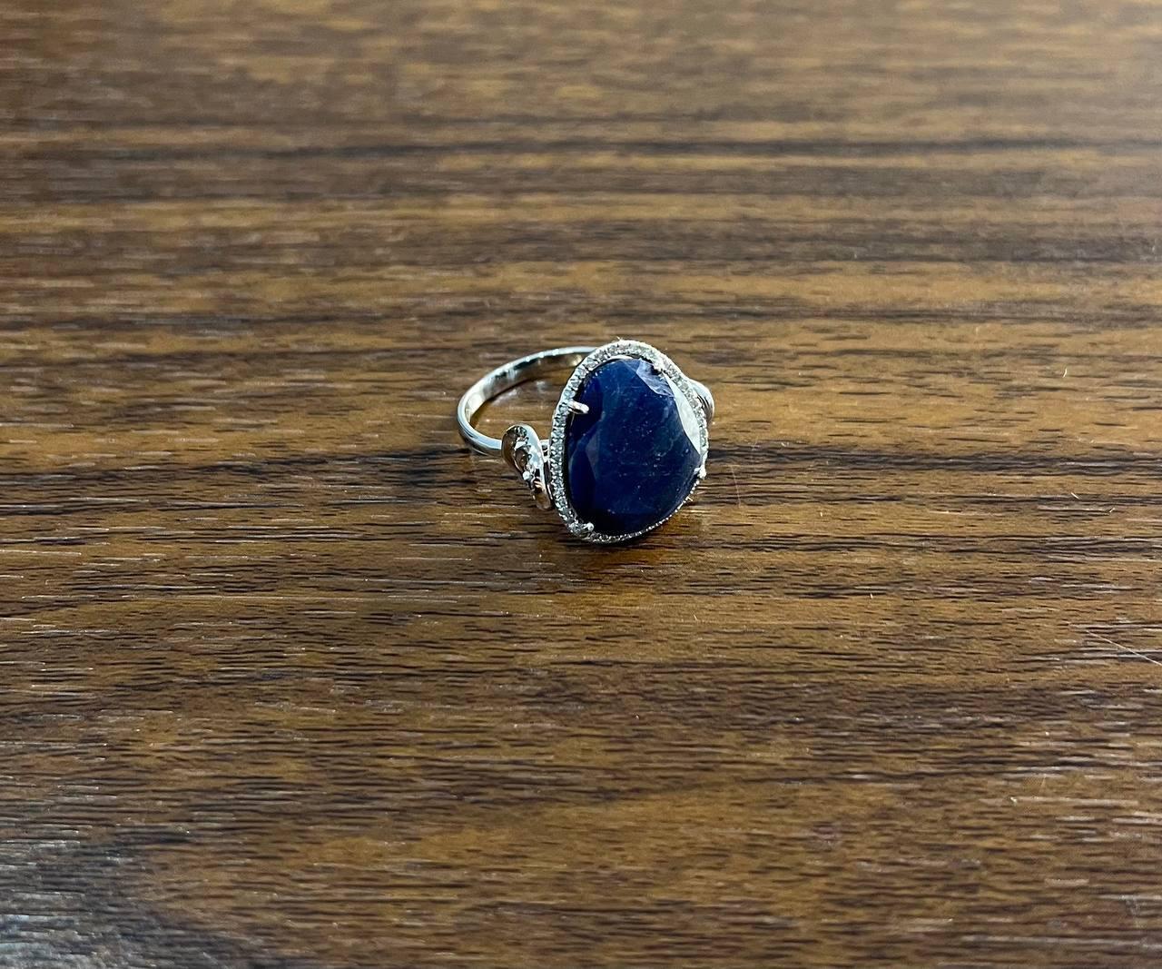 This piece features a large, teardrop-shaped dark blue sapphire, set in a delicate 14K white gold band. 27 x 20 mm size

The stone is surrounded by a halo of small, sparkling diamobd accents, enhancing its deep color.

A sophisticated accessory that