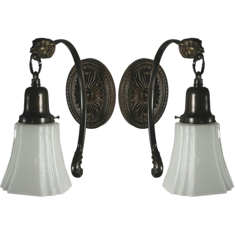 #2-1075 a dark brass one arm sconce ending with a ram head supporting a milk glass shade.
One piece available.

  