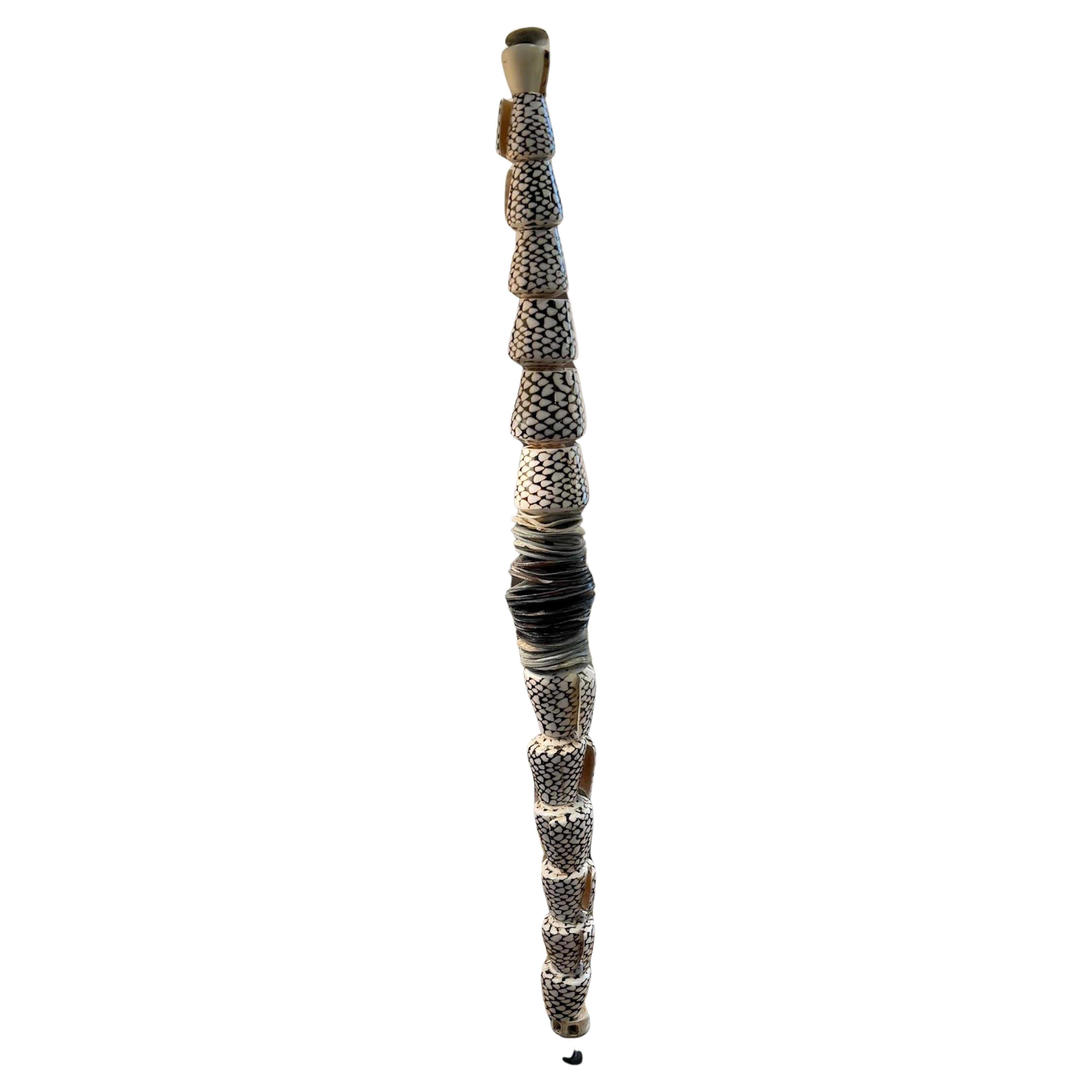 Contemporary Indonesian stack of polished shells on stand.
Decorative hand painted dark brown and cream circular pattern design.
Interspersed series of flattened shell rings in shades of slate blue.
Solid cream shell with a beaded shell at the top.