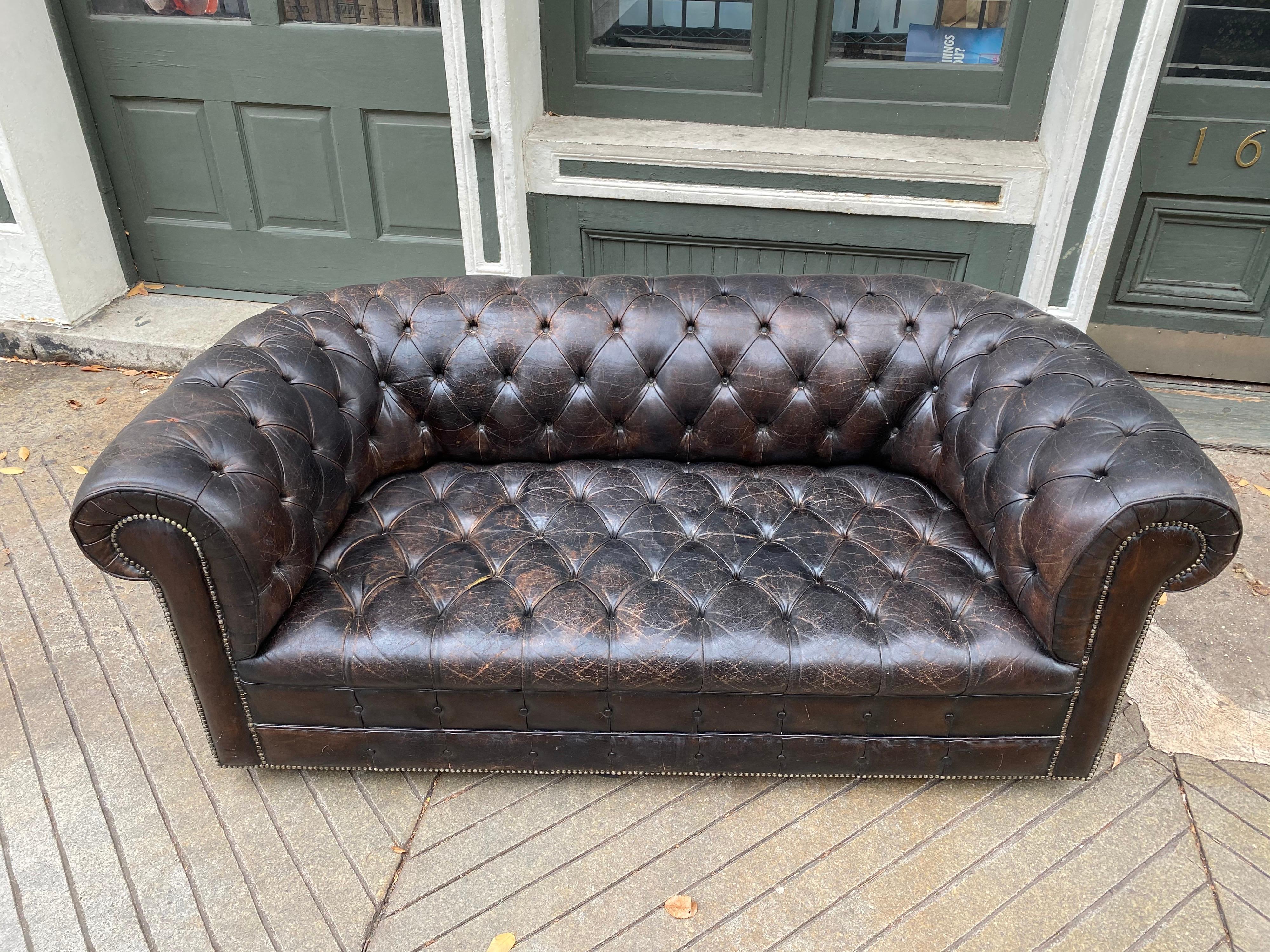 Chesterfield dark brown leather loveseat, dating from the late 1970s or early 1980s. Well worn and loved. Shows 40 plus years of use. Overall Patina is really nice. Three spots as shown in photos where there are small tears to leather. One button