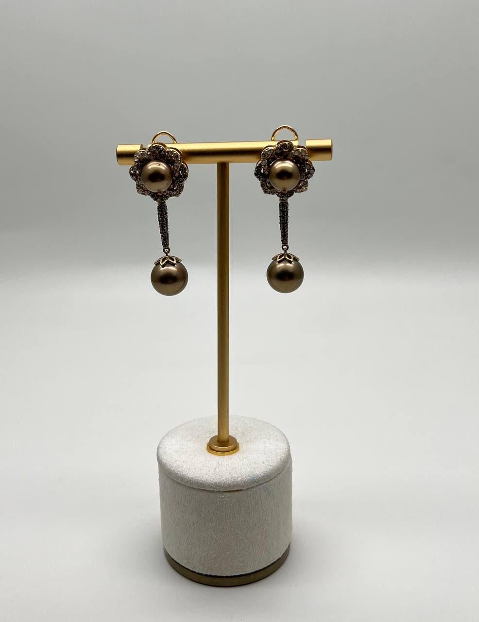 Discover the elegance of these cluster dangle earrings.

Featuring a captivating design with intricate floral clusters, each earring is adorned with a central pearl surrounded by shimmering diamonds.

A delicate chain suspends a single pearl, adding