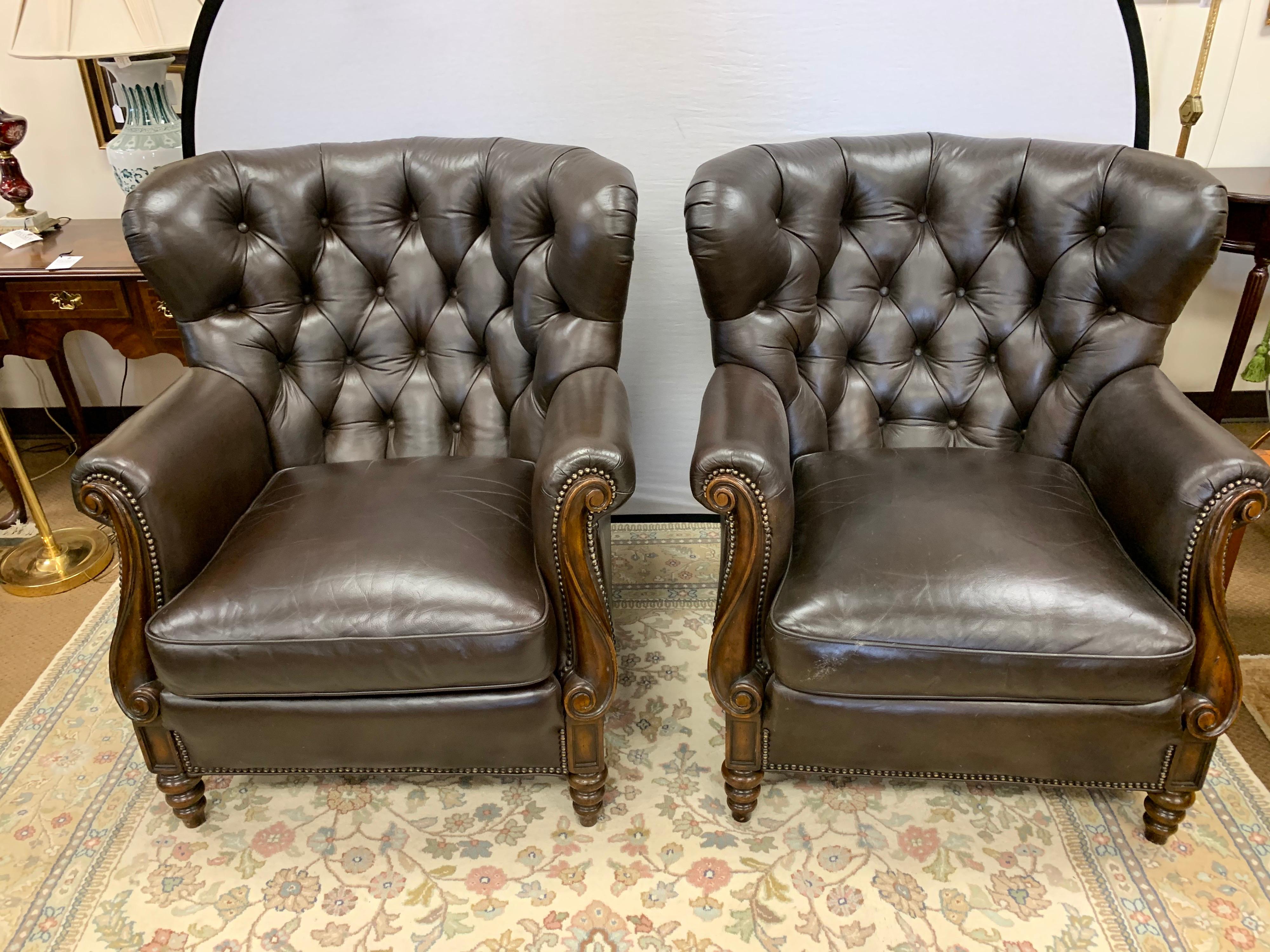 Handsome pair of matching Chesterfield tufted leather chairs with carved mahogany wood detail on arms and legs. Finished with brass nailheads all around. Super comfy for your library office or family room.
