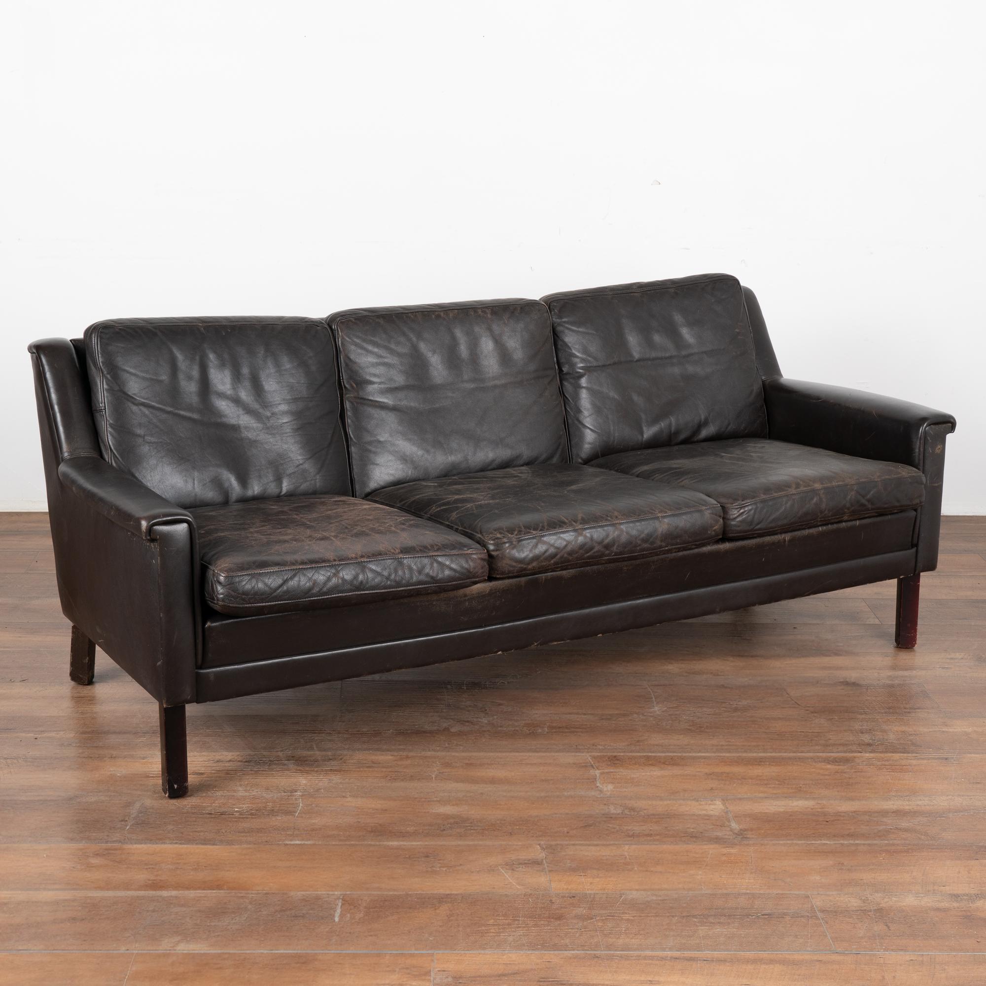 Mid-century modern dark chocolate brown leather three-seat sofa with removable cushions and hard wood frame.
The years of use are revealed in the aged patina of the leather, including impressions, scuffs/scratches, some discoloration, stains on