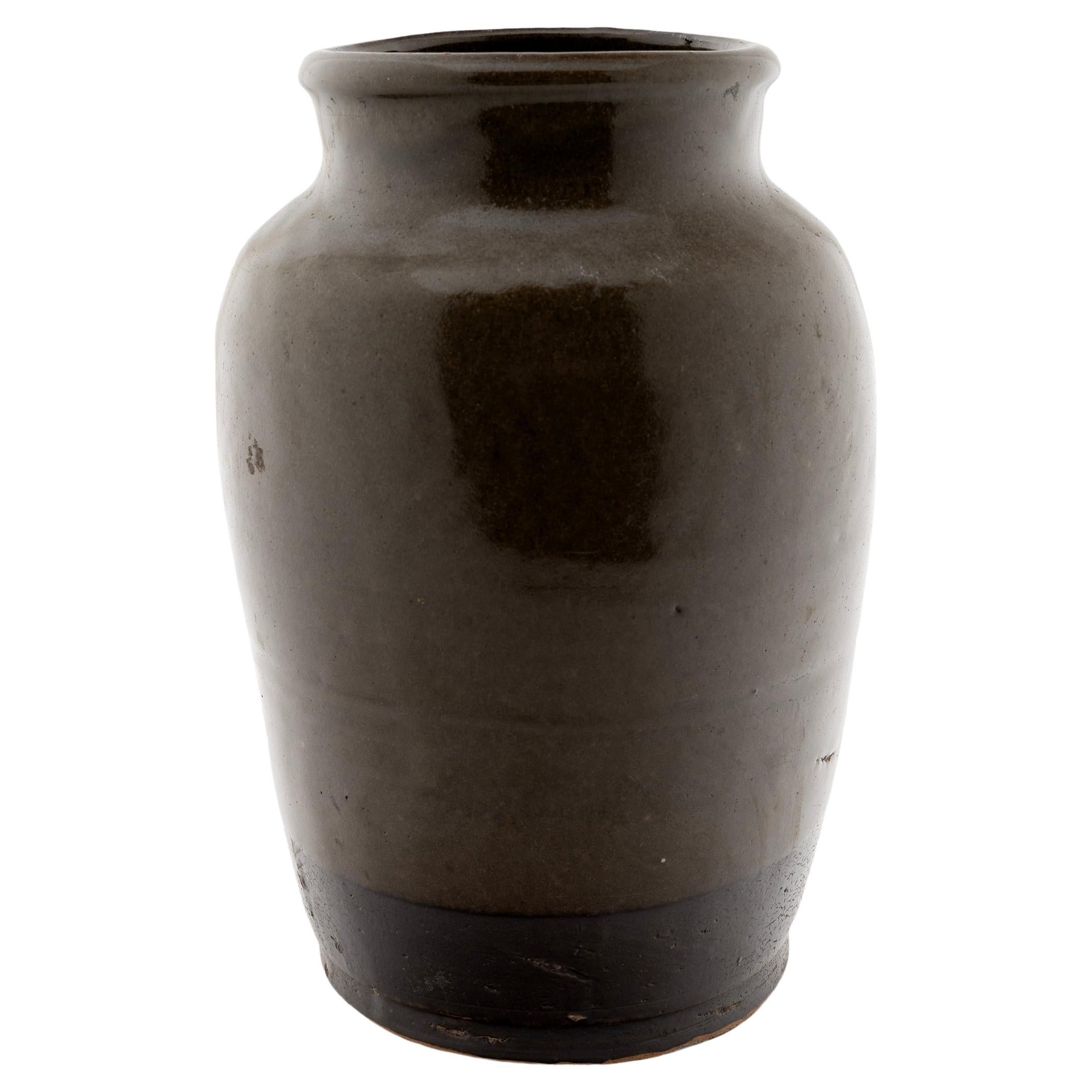 A lustrous brown glaze coats the slender tapered form of this late 19th-century kitchen jar. As evidenced by the glazed interior, the jar was once used daily in a Qing-dynasty kitchen for fermenting foods and condiments. The tapered jar features