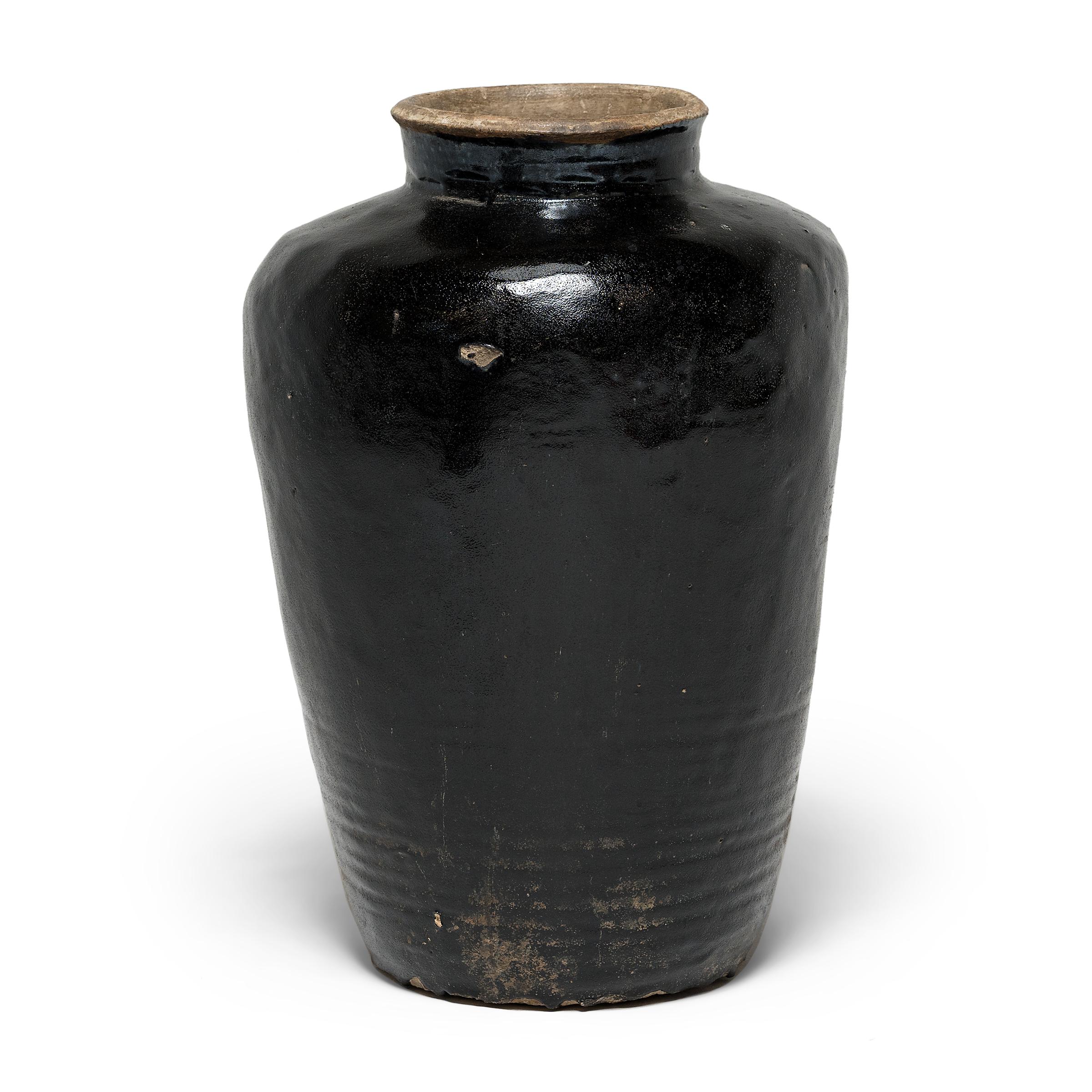This large stoneware vessel is a Qing-dynasty wine jar, used to store wine and spirits made from rice and other grains. The large vessel would have been sculpted by hand, and bears traces of the maker’s hand in its irregular surface. The subtle