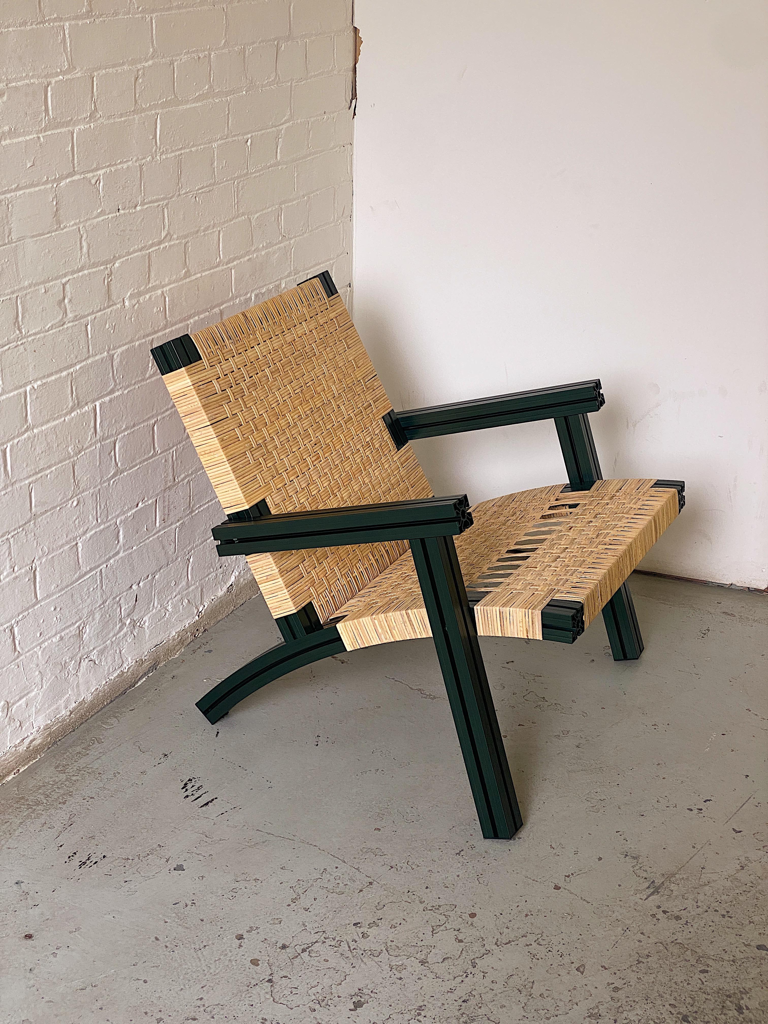 Armchair made from dark green anodised aluminium extrusions and woven cane seating.

Originally realised for the Hepworth Gallery in Wakefield and inspired by Donald Judd and Børge Mogensen, Anodised Wicker marries industrially extruded and anodised