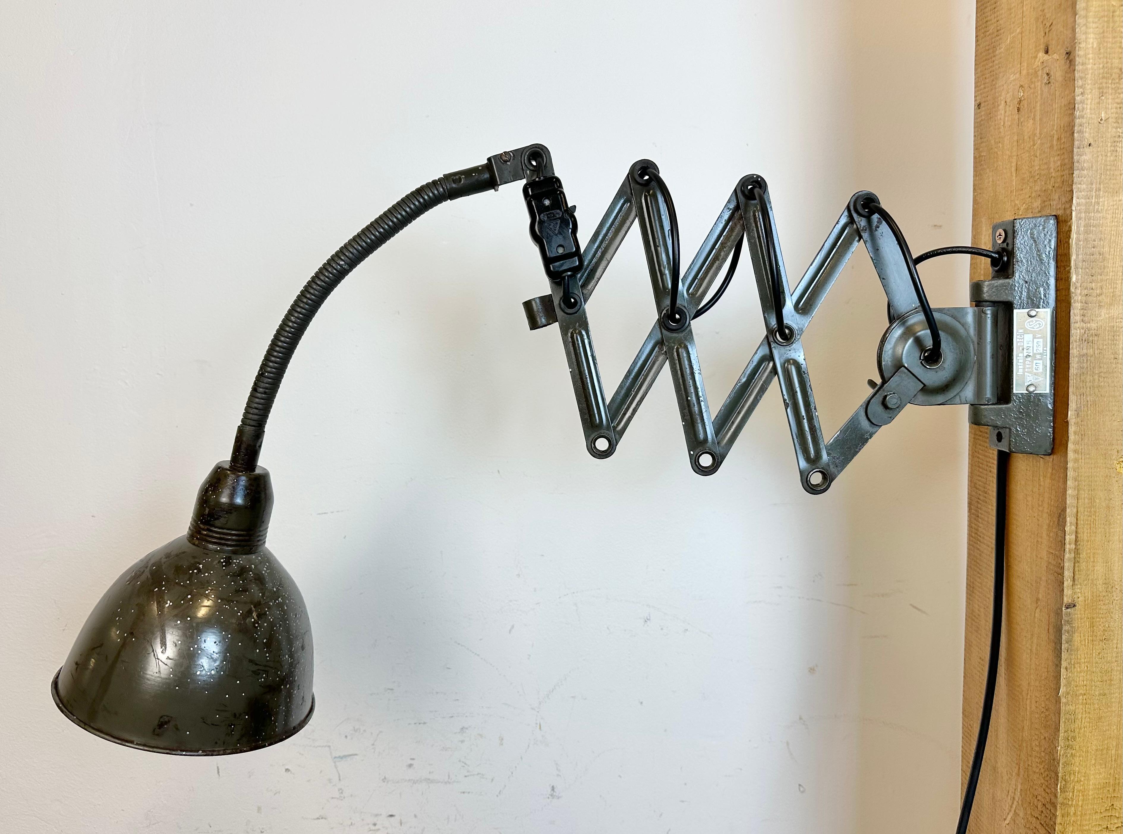 This vintage Industrial dark green scissor wall light was produced by Elektroinstala Decín in former Czechoslovakia during the 1960s. It has a metal lampshade. The iron scissor arm is extendable and can be turned sideways. The socket requires E 27/