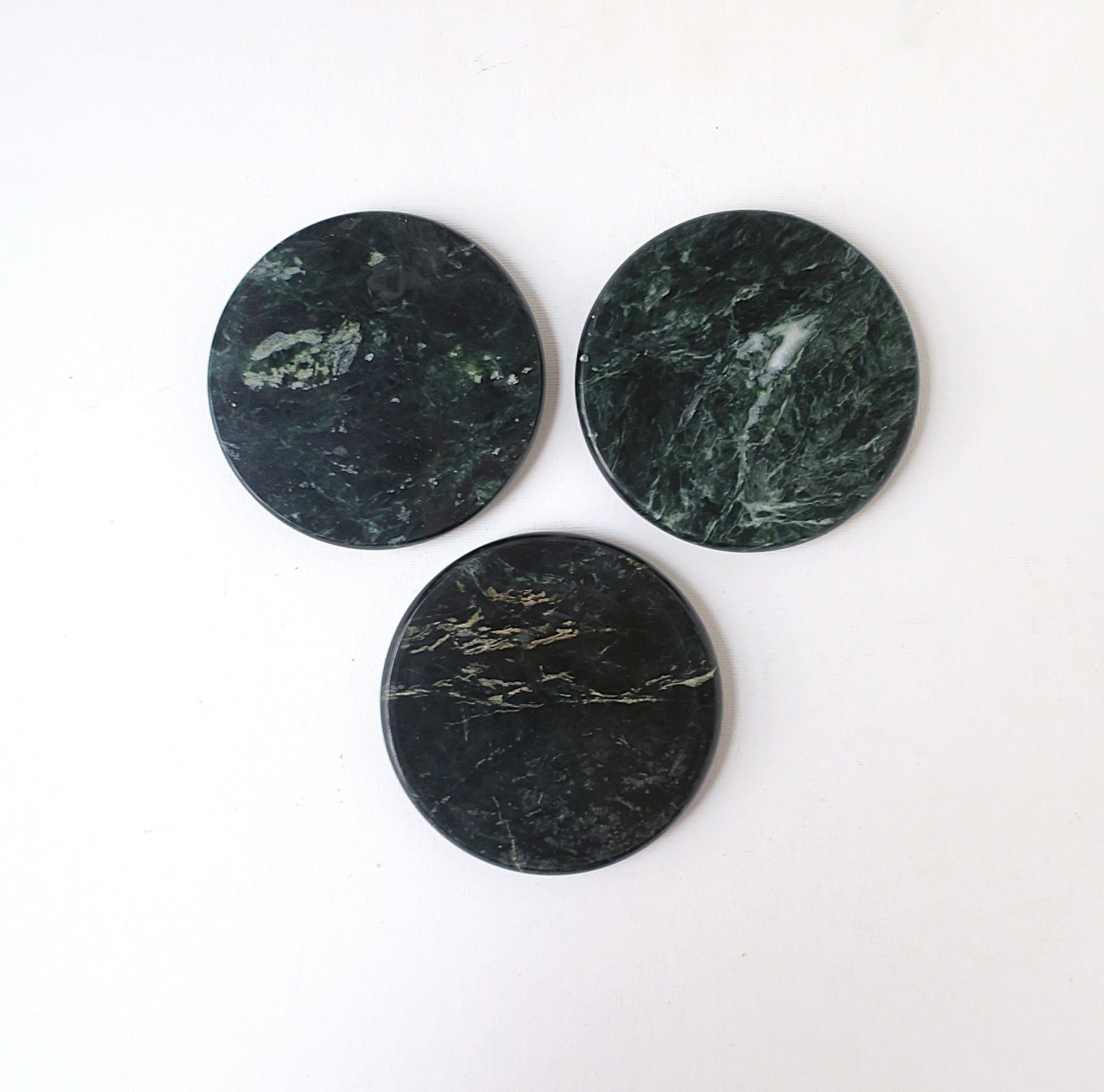 A set of three (3) round dark green marble coasters for drinks, cocktails, champagne, etc., modern style/Postmodern period, circa late-20th century. Coasters are dark green with white veining, one with traces of tan, soft edge, polished smooth, cork