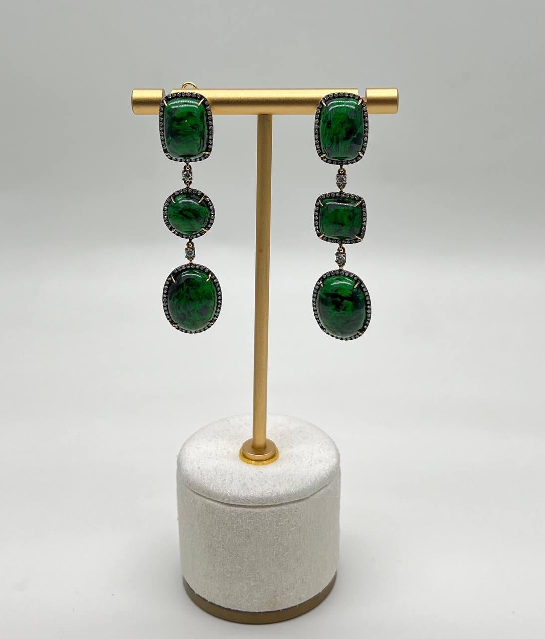 Elegant 18k Gold Green Maw Sit Sit Drop Earrings. These stunning earrings feature vibrant green gemstones set in a luxurious 18k gold frame. The design showcases three descending stones, each surrounded by a delicate halo of smaller diamonds ,
