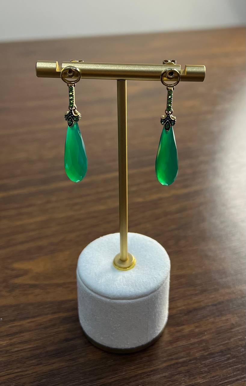 Cada pendiente presenta un cuarzo verde talla pera, suspendido de un delicado engaste adornado con gemas verdes más pequeñas y daimantes.

El diseño es a la vez moderno y sofisticado, con un acabado suave y pulido que capta la luz maravillosamente.