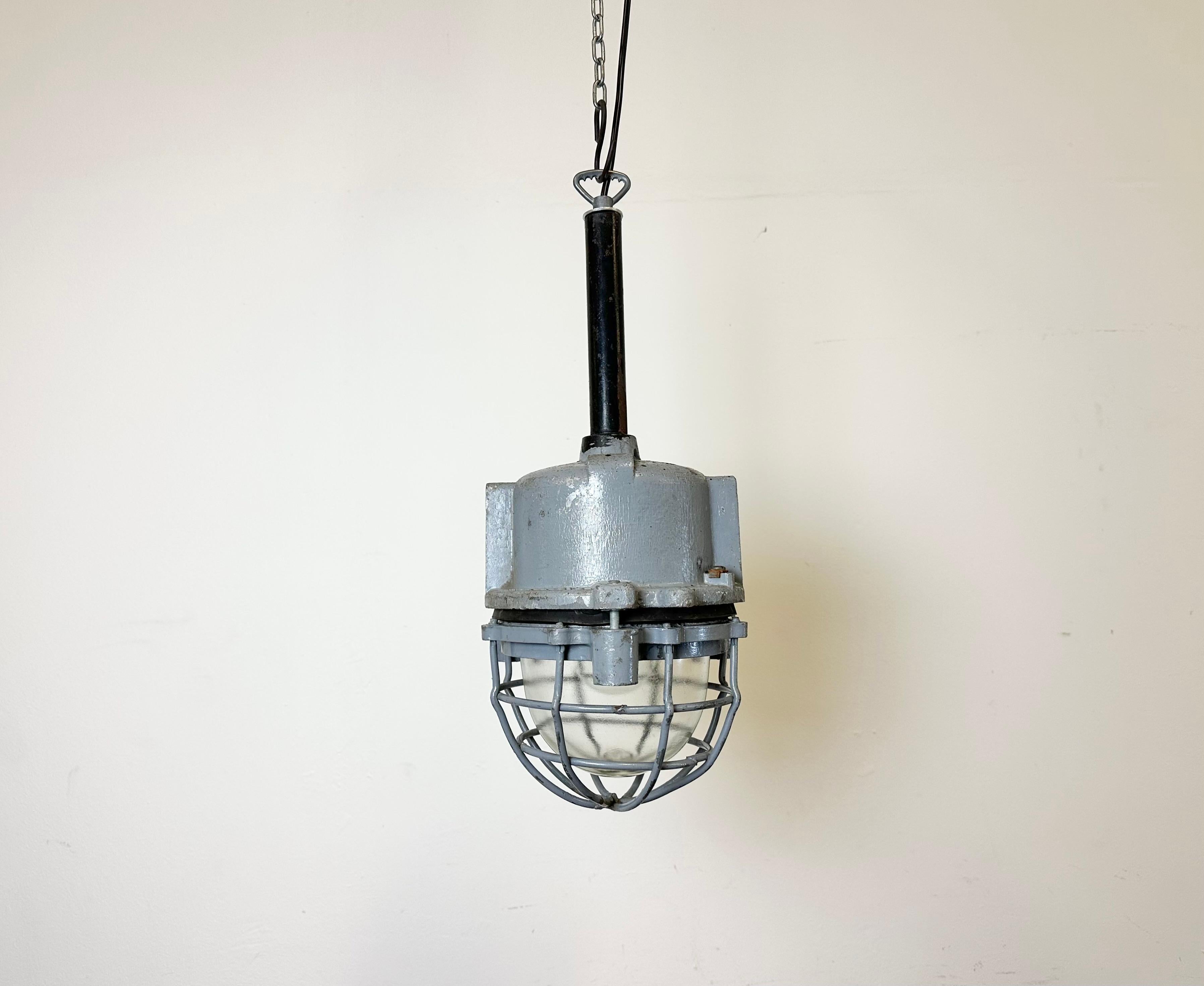 Dark grey industrial lamp with massive protective glass bulb made by ELBA in Romania during the 1970s.It features a cast aluminium body, a black iron suspension ,an explosion proof clear glass cover and an iron protective grid.Porcelain socket