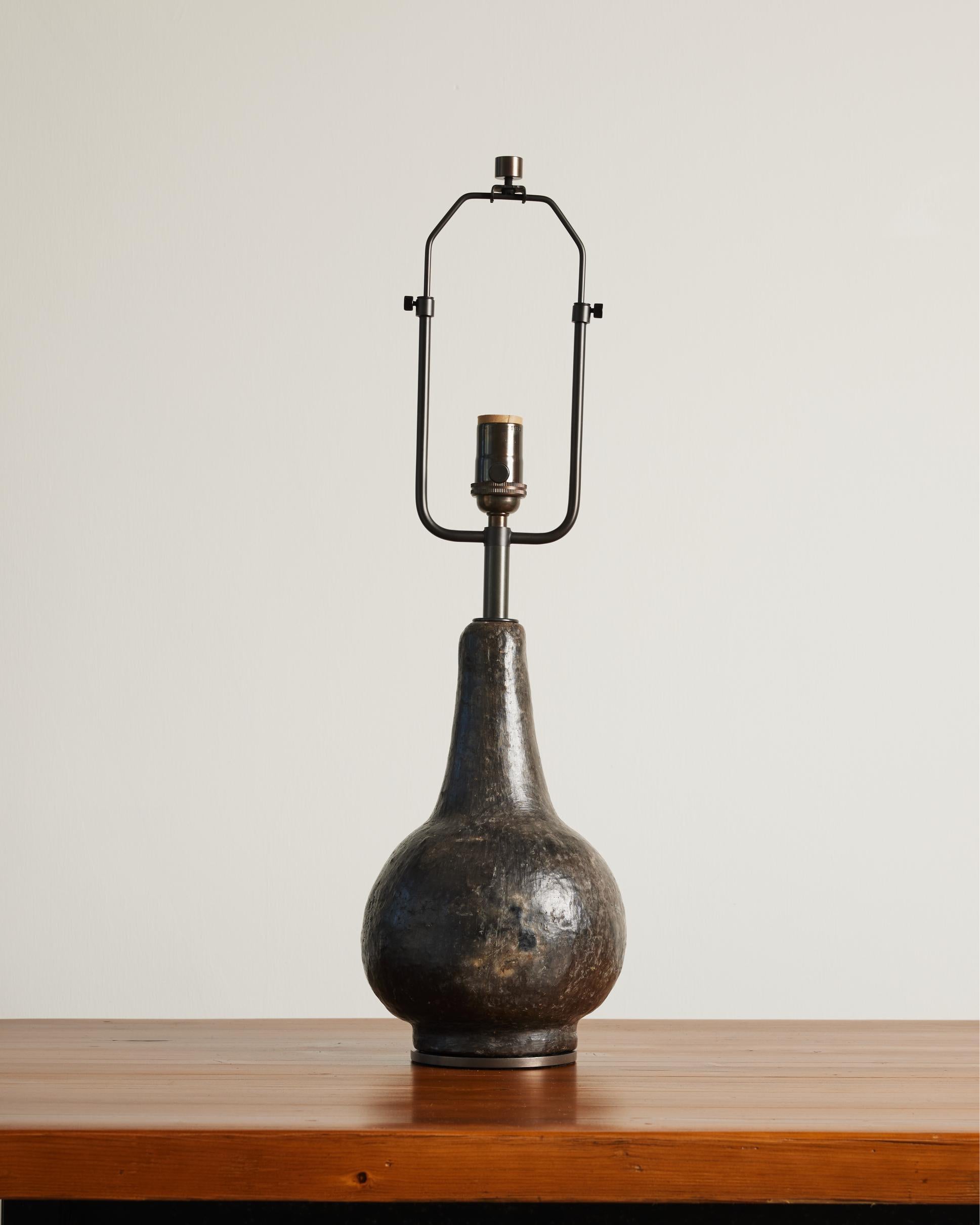 Ceramic table lamp with textured, multicolored glaze and a patinated bronze base.
This lamp boasts a pear-shaped silhouette and would sit well in a moody study or as a bold accent on a nightstand.

The lamp features an adjustable harp, with the
