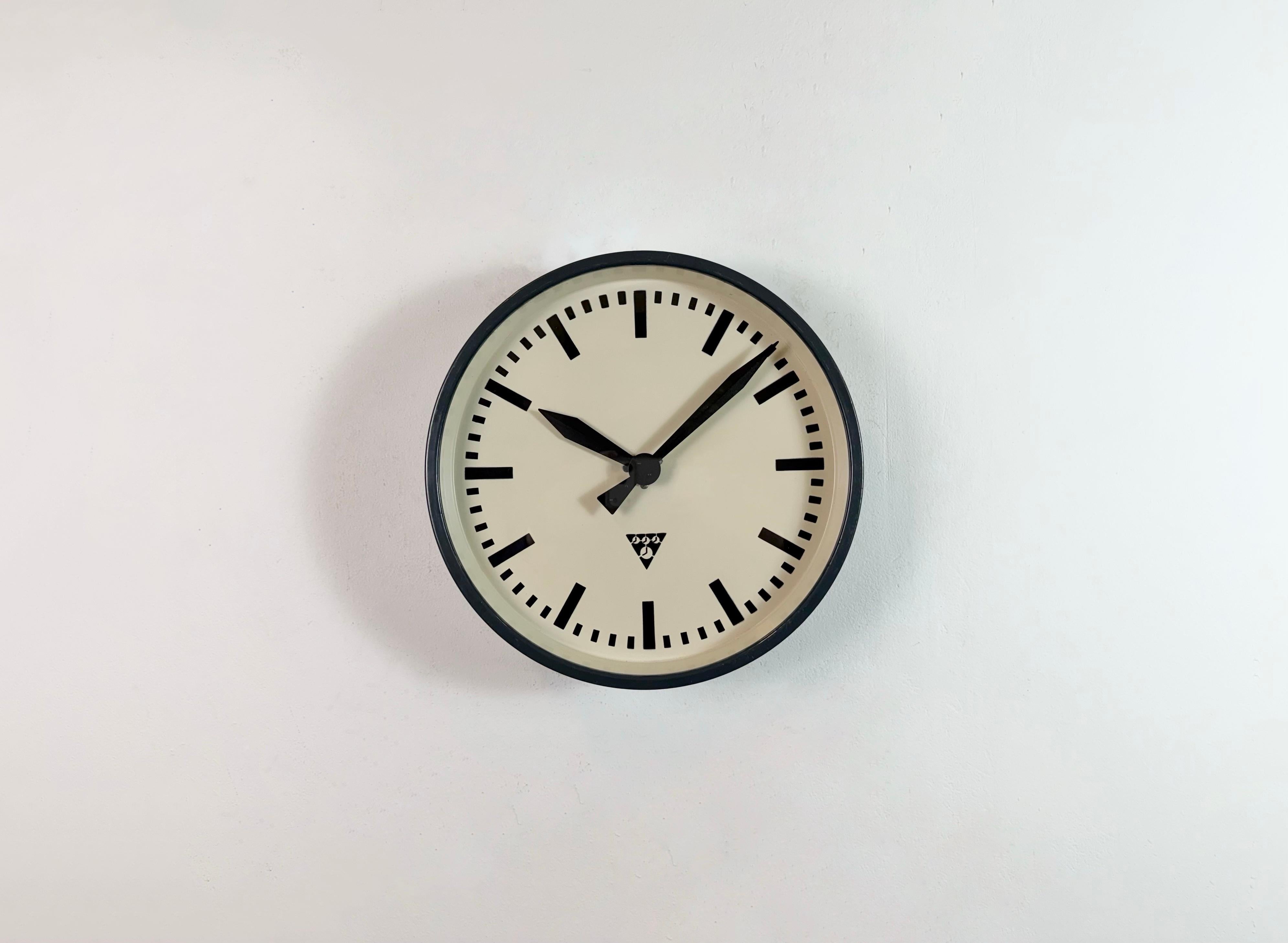 This wall clock was produced by Pragotron in former Czechoslovakia during the 1960s. It features a dark grey metal frame, an iron dial, an aluminium hands and a clear glass cover. The former factory electric slave clock has been converted into a