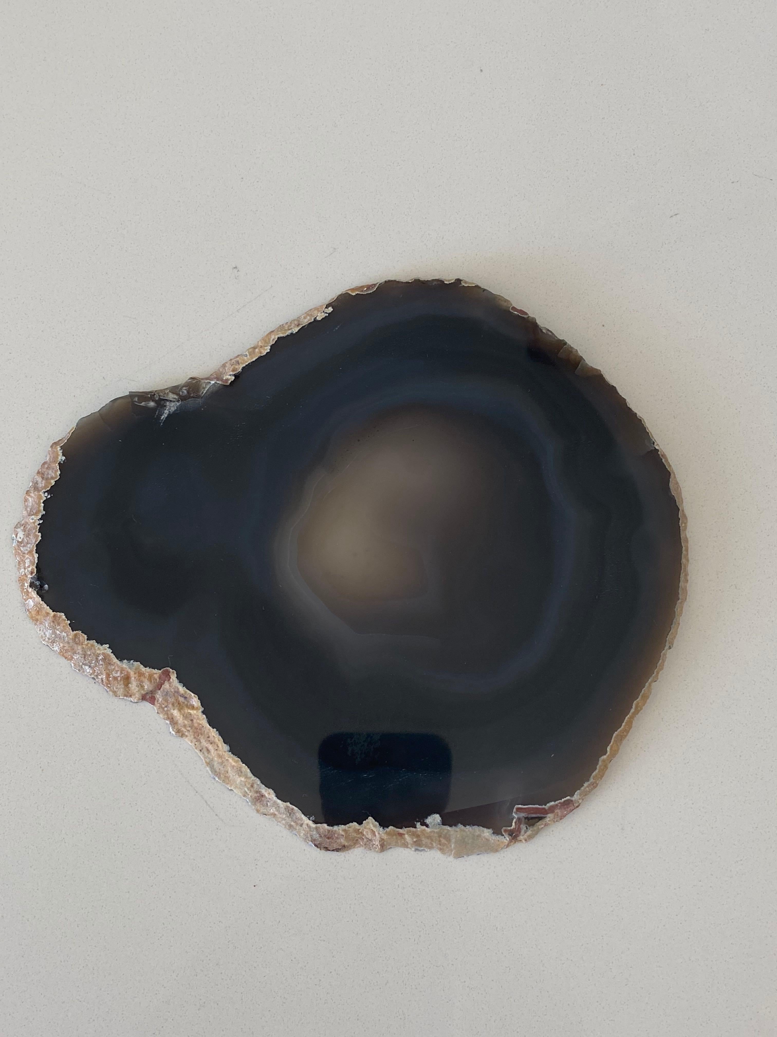 Brazilian thin slice of dark grey agate mounted on a wood stand.
Agate is a banded form of finely-grained, microcrystalline Quartz. 
The lovely color patterns and banding make this translucent gemstone very unique. 
Agates can have many