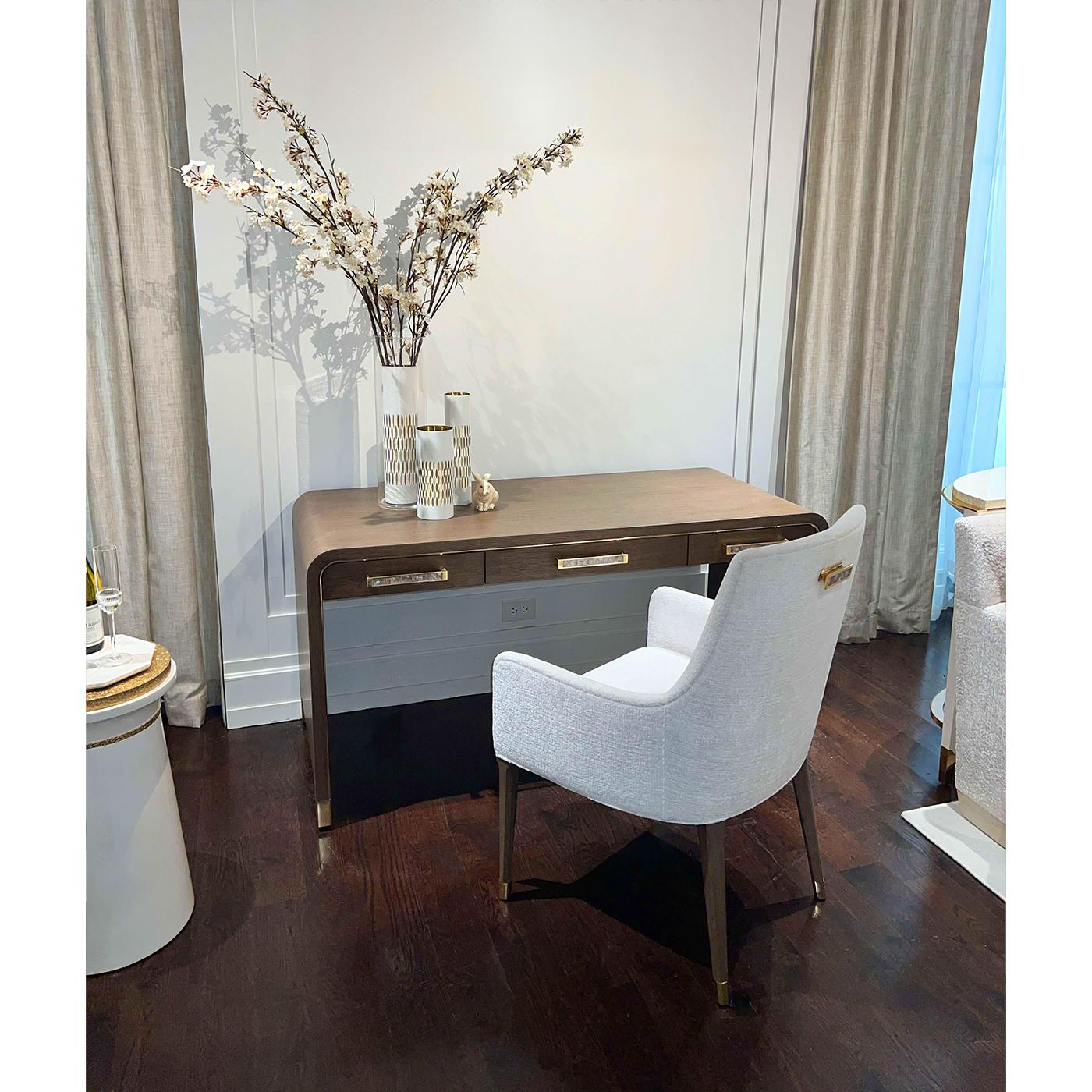 Dieser Schreibtisch verbindet zeitlose Form mit luxuriösen Details. Seine elegante Wasserfall-Silhouette wird durch abgerundete Ecken abgemildert und ist in ein warmes Nerzholz-Finish gehüllt. Poliertes Messing umrahmt den Rahmen, während