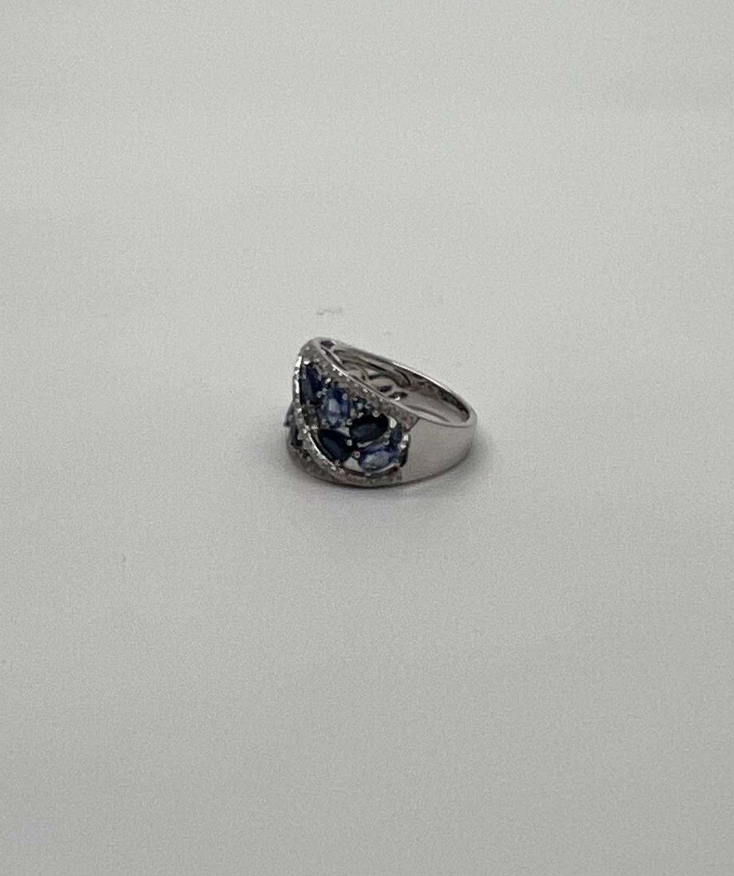 This elegant ring features a striking design with deep blue sapphires set in a wide band. The gemstones are arranged in a pattern that intertwines with sparkling accent diamonds, creating a captivating visual effect. The band is substantial,