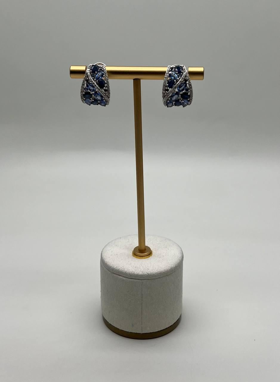 These exquisite earrings feature a stunning design with intricate detailing. The earrings showcase a beautiful arrangement of blue sapphires, elegantly intertwined with shimmering diamonds. Crafted with precision, they offer a sophisticated and