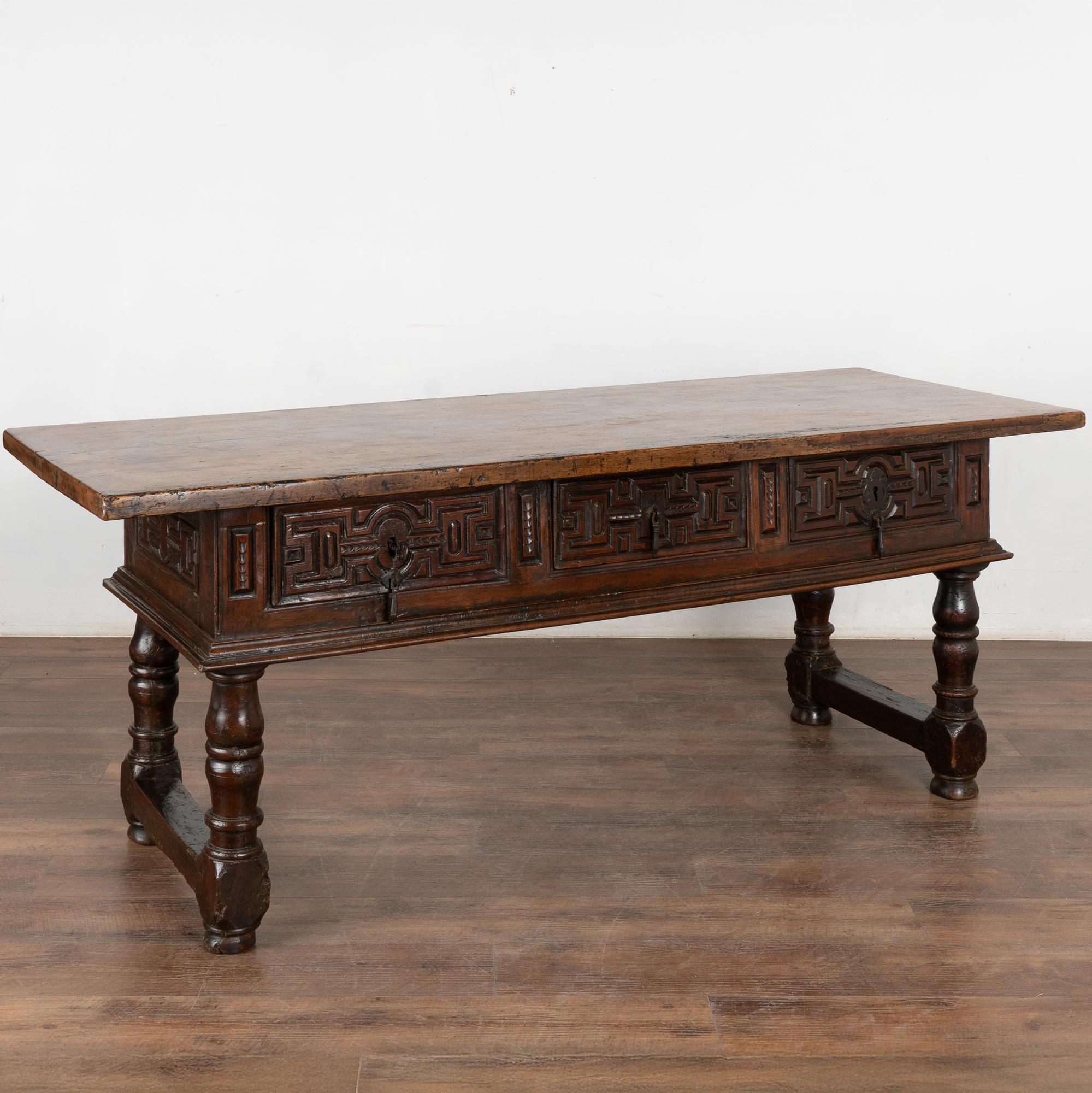 Dark walnut console table with three drawers resting on heavy turned legs from Spain. Note the solid piece of wood that forms the handsome top and deep carving along each drawer front.
Please enlarge photos (especially of top) to appreciate the dark