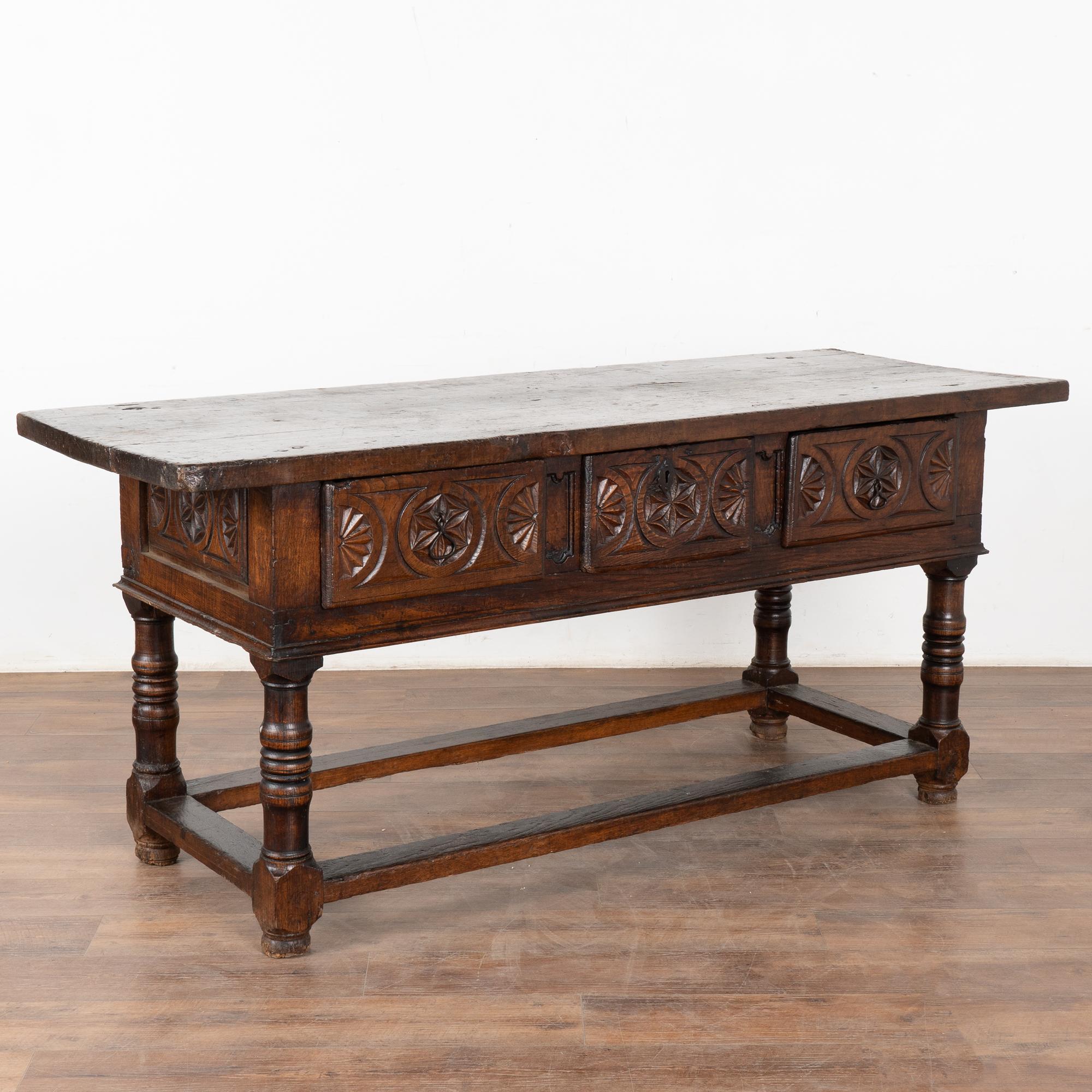 Dark oak console table with three drawers resting on trestle base from Spain. Note the deep carving along each drawer front.
Please enlarge photos (especially of top) to appreciate the dark patina of the wood, including old cracks, gouges, stains