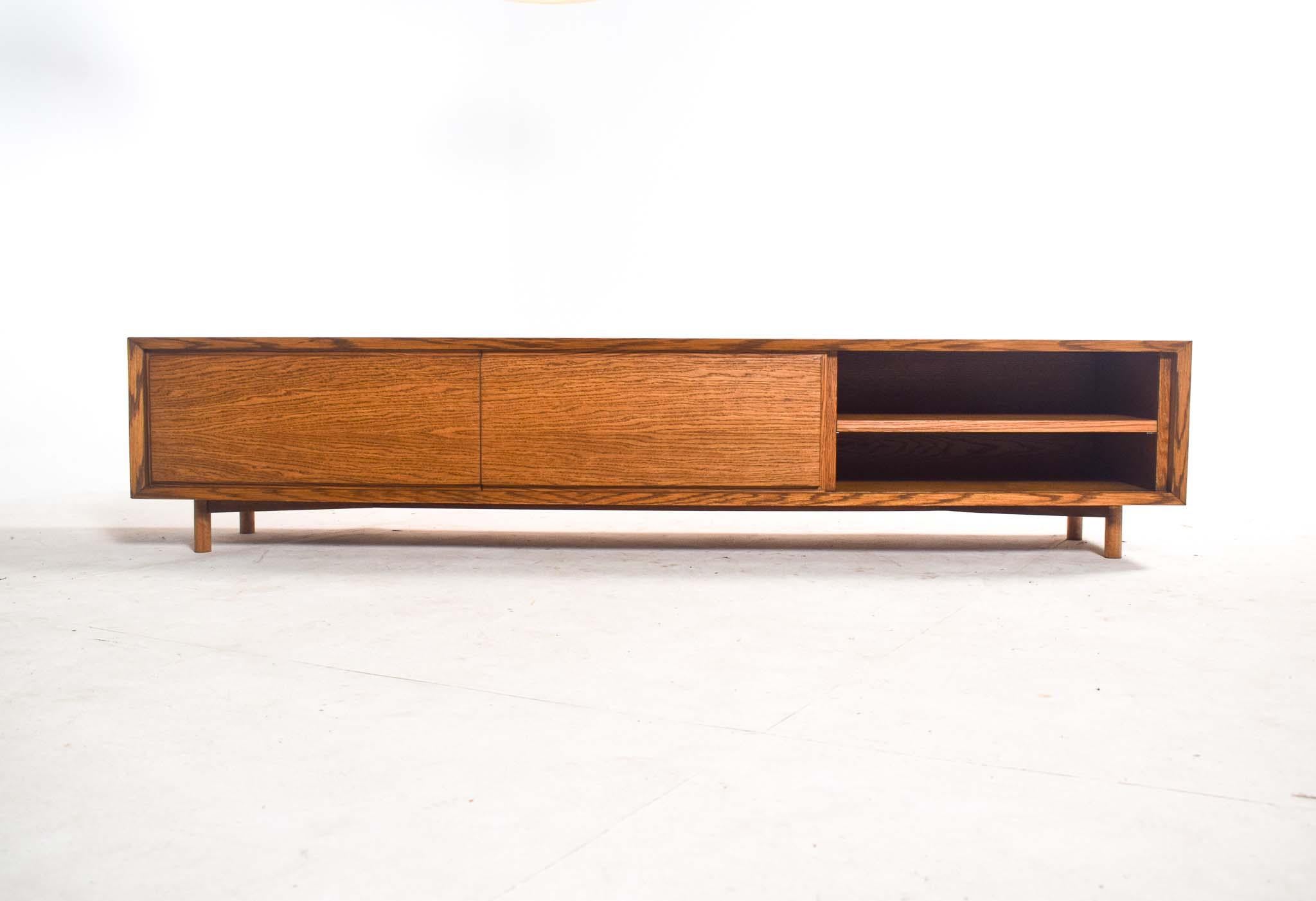 This elegant low-profile sideboard features a minimalist design crafted from dark oak wood with a warm, natural oil finish that highlights its rich grain pattern. It includes two sliding doors for concealed storage, combining functionality with
