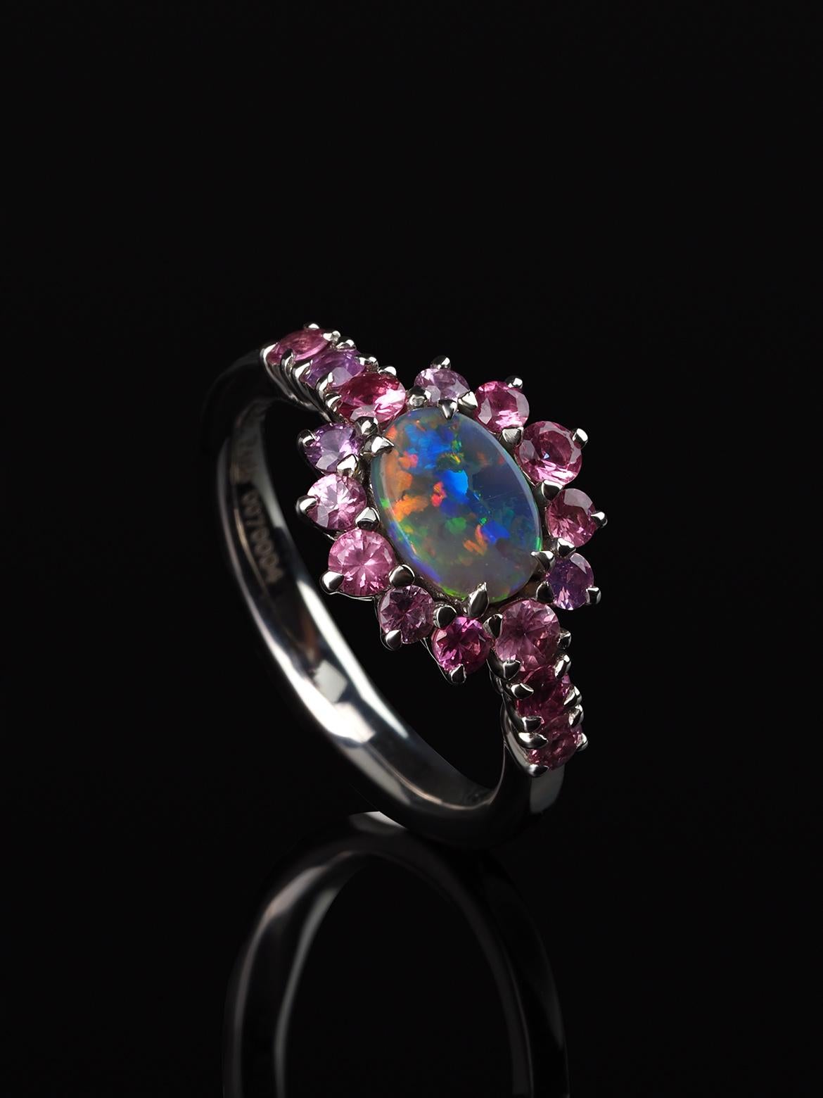 This contemporary custom made engagement ring/promise ring features a unique interplay of naturally beautiful gemstones. An Australian Opal is securely prong set sideways in the center, exhibiting an incredible play-of-color rainbow. This