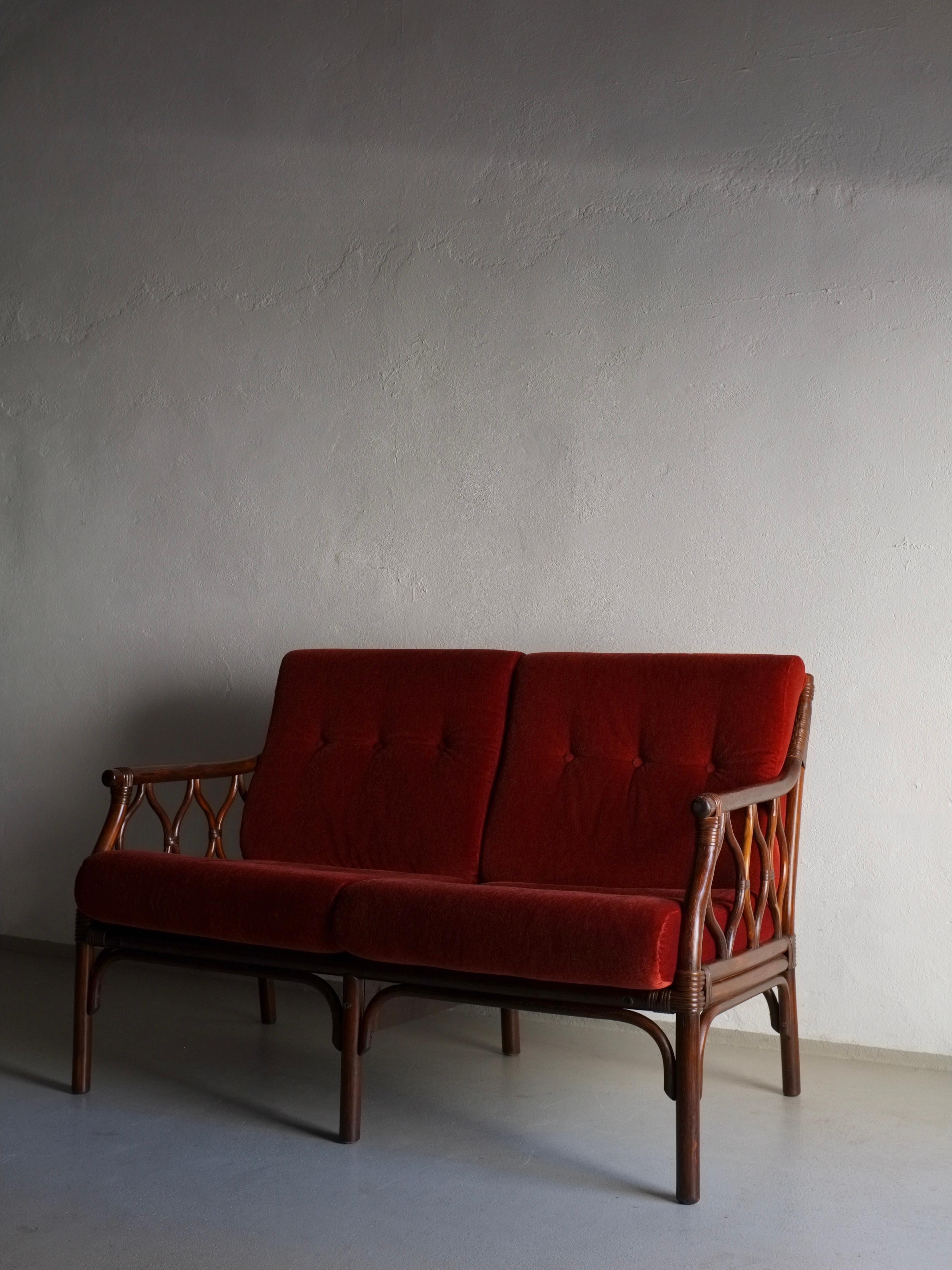 Canapé 2 places en rotin foncé avec cautions en velours rouge-orange vermillon. Un canapé 3 places, une chaise longue et une table basse de cet ensemble sont disponibles.

H(total/cadre) 84/77 cm, h(assise) 44 cm, L 122 cm, P 75 cm