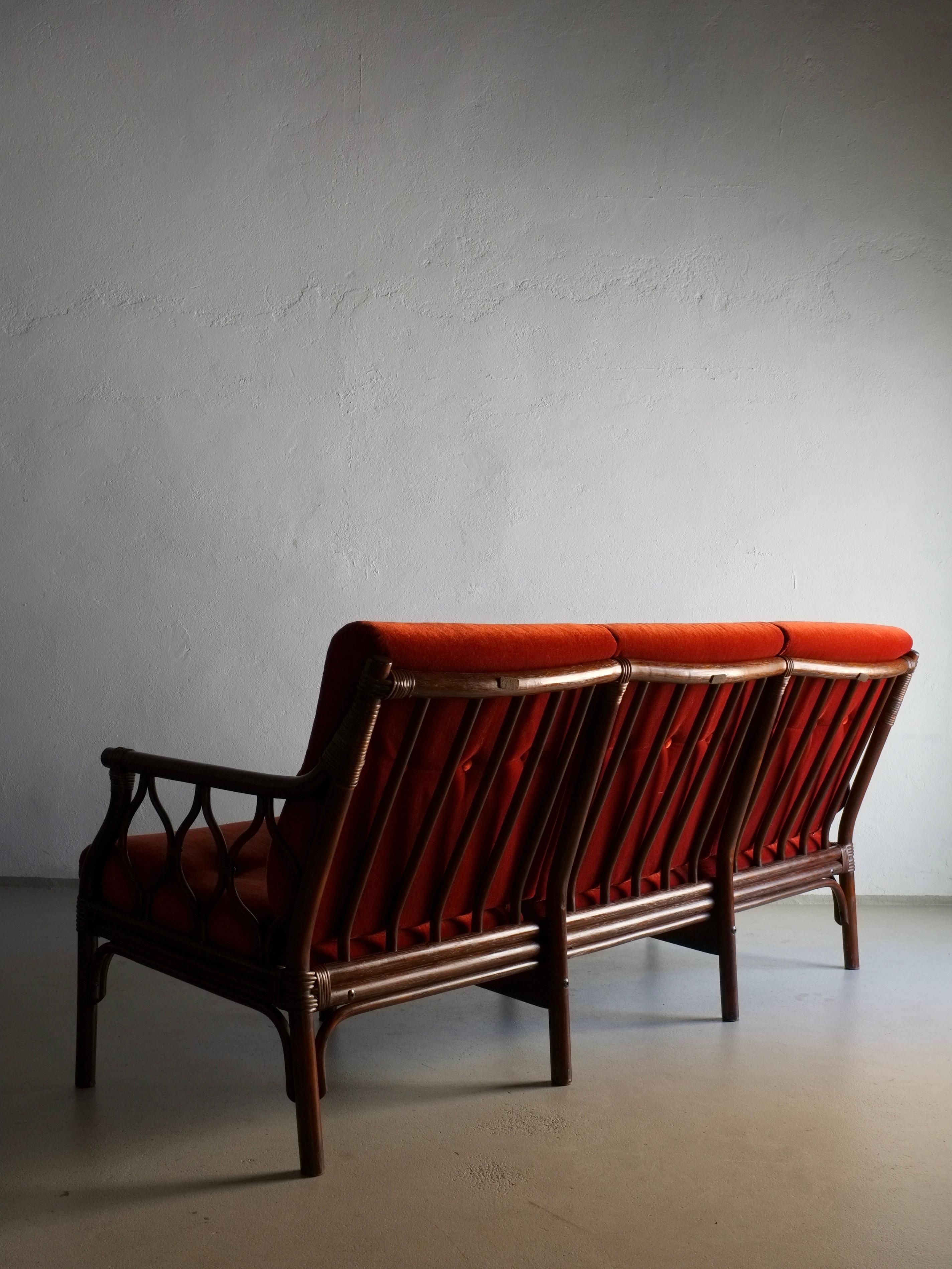 3-Sitzer-Sofa aus dunklem Rattan mit zinnoberrotem Veloursbezug. Ein 2-Sitzer-Sofa, ein Sessel und ein Couchtisch aus diesem Set stehen zur Verfügung.

H(gesamt/Gestell) 84/77 cm, H(Sitz) 44 cm, B 180 cm, T 75 cm

