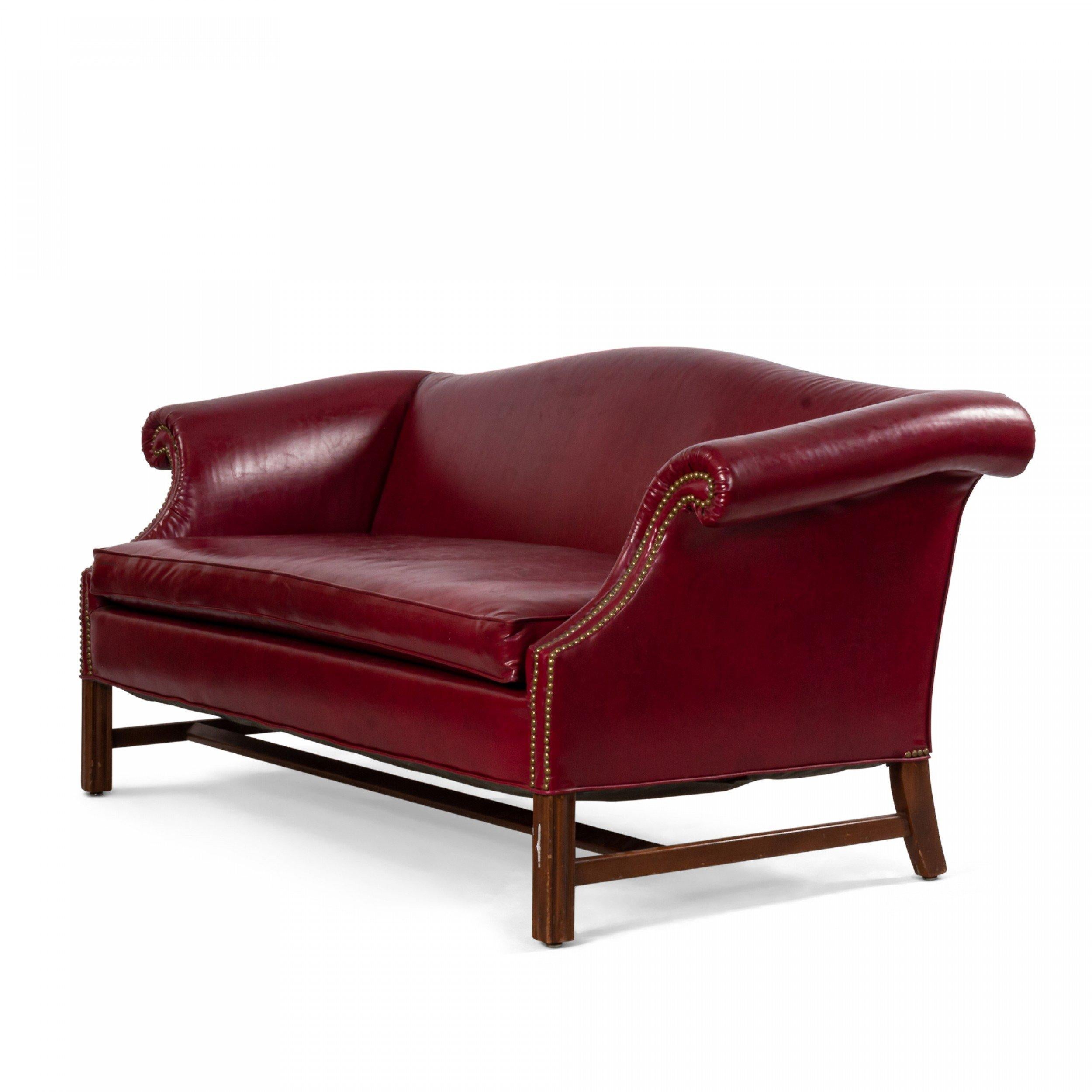 Vintage English Georgian style red leather camelback chesterfield sofa with out-scrolled arms with brass nail head trim & a red leather seat cushion supported on straight reeded legs connected by a center stretcher with a single seat cushion
 